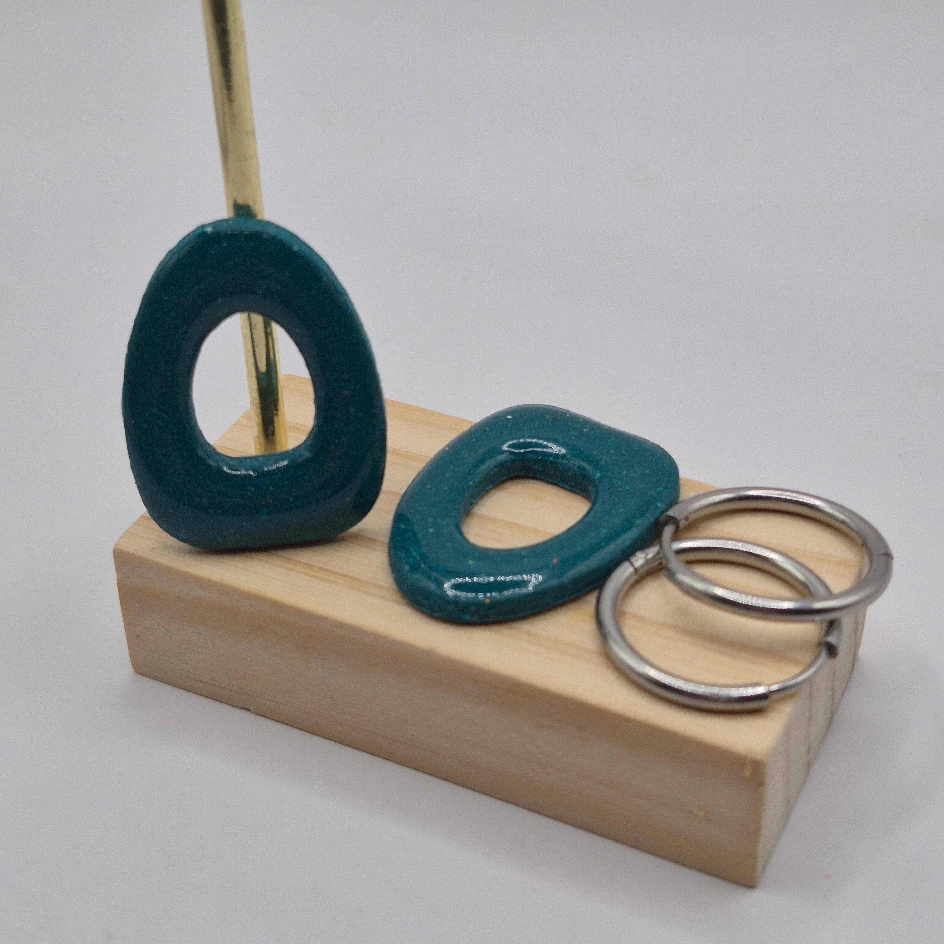 Parure Cynthia : pampilles interchangeables en pâte polymère rouge et blanc, en forme géométrique de triangle arrondi, présentées sur un support en bois avec deux créoles en acier inoxydable argentées.