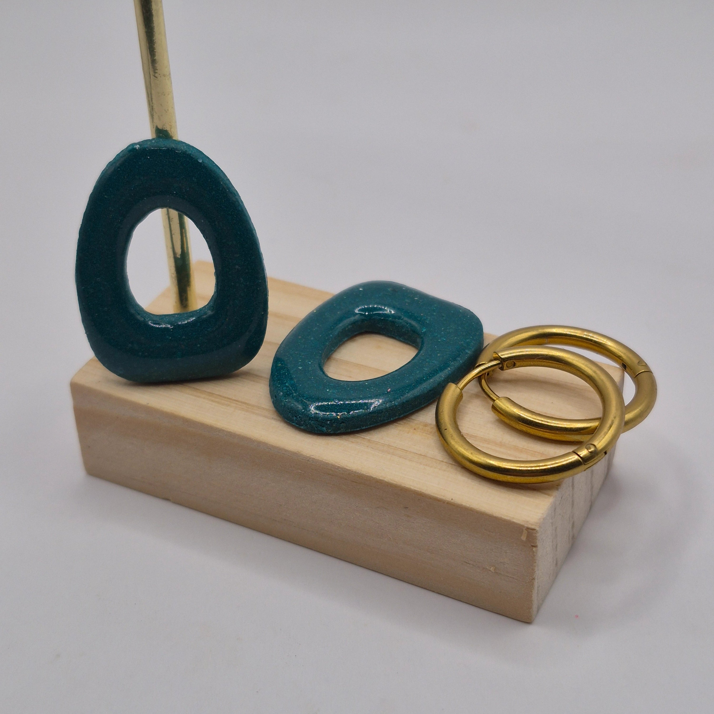 Parure Cynthia : pampilles interchangeables en pâte polymère rouge et blanc, en forme géométrique de triangle arrondi, présentées sur un support en bois avec deux créoles en acier inoxydable dorées.