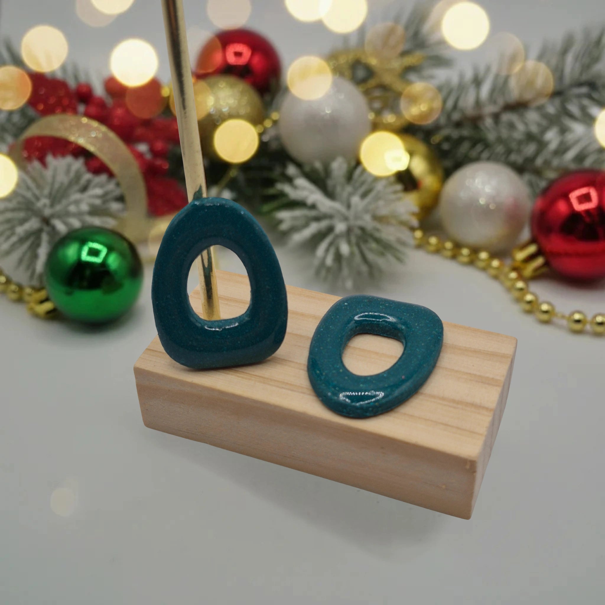 Parure Cynthia : pampilles interchangeables en pâte polymère rouge et blanc, en forme de fleur, présentées sur un support en bois, et en arrière-plan des branches de sapin, des guirlandes et des boules de Noël.