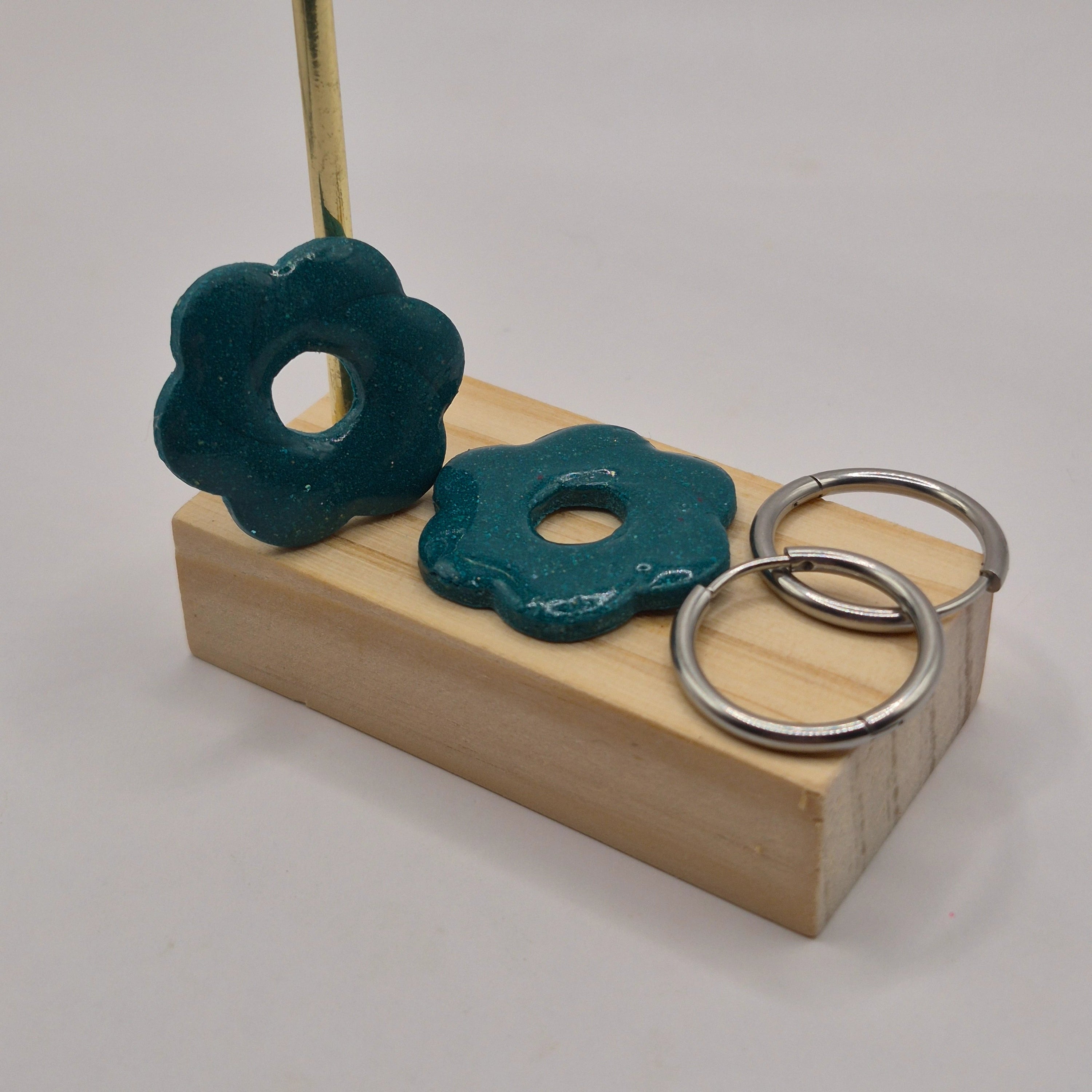 Parure Iris : pampilles interchangeables en pâte polymère vertes pailletées, en forme de fleur, présentées sur un support en bois, avec deux créoles en acier inoxydable argentées.