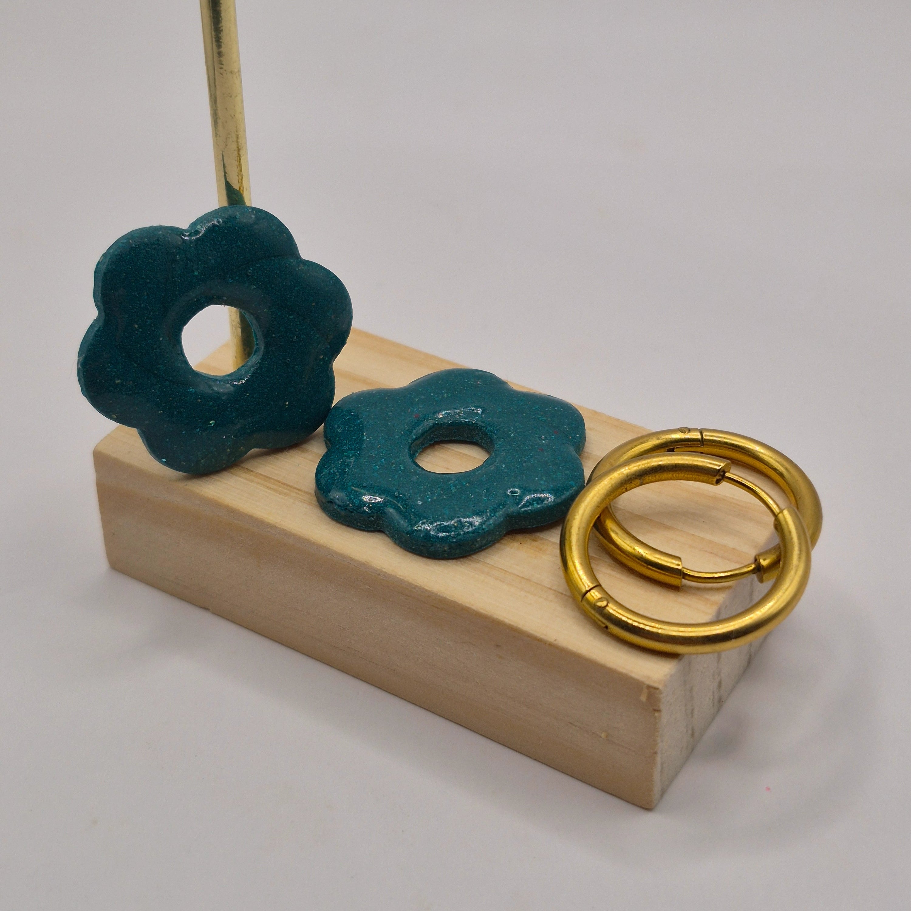 Parure Iris : pampilles interchangeables en pâte polymère vertes pailletées, en forme de fleur, présentées sur un support en bois, avec deux créoles en acier inoxydable dorées.