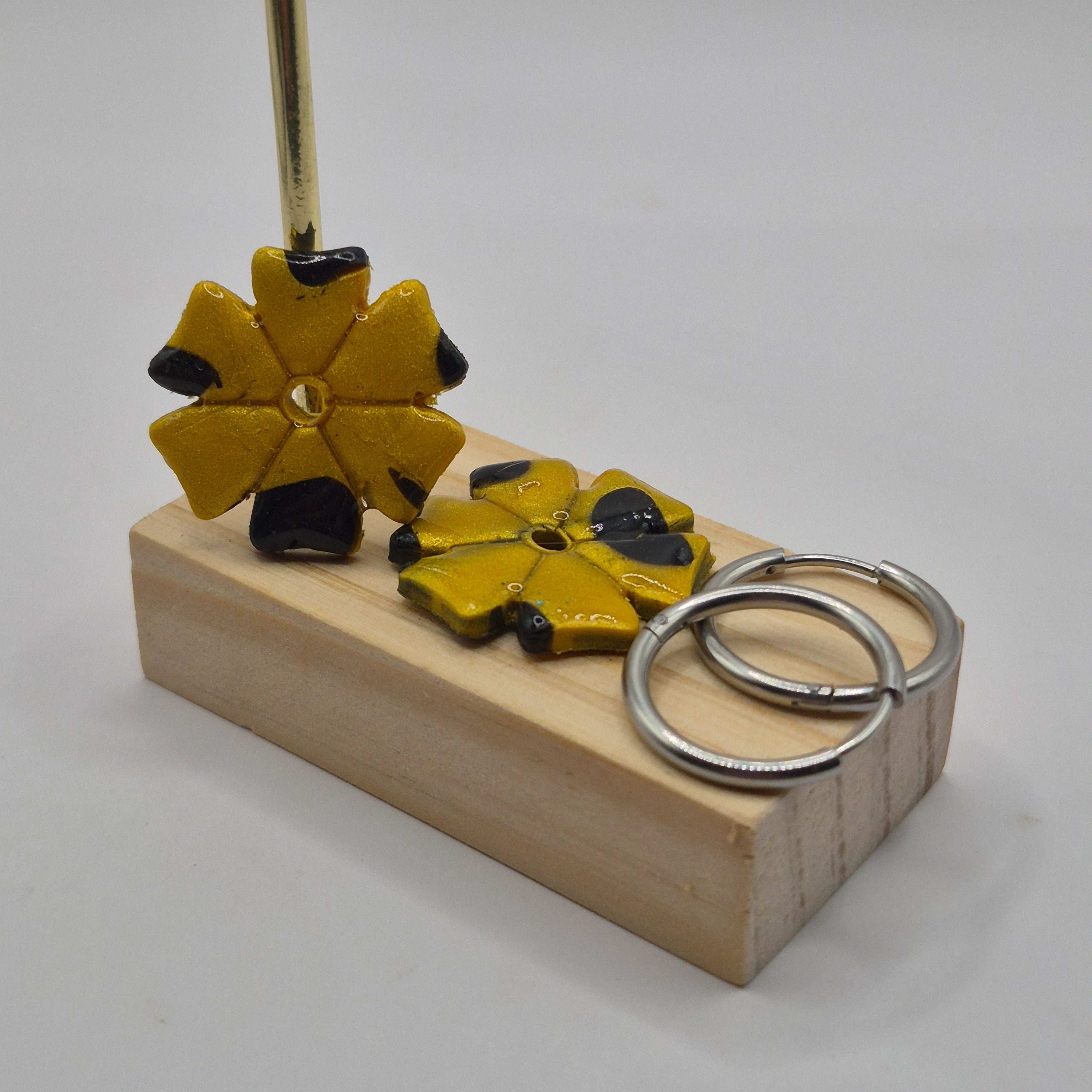 Parure Jessica : pampilles interchangeables en pâte polymère doré et noir, en forme de trèfle à 6 feuilles, présentées sur un support en bois, avec 2 créoles en acier inoxydable argentées.