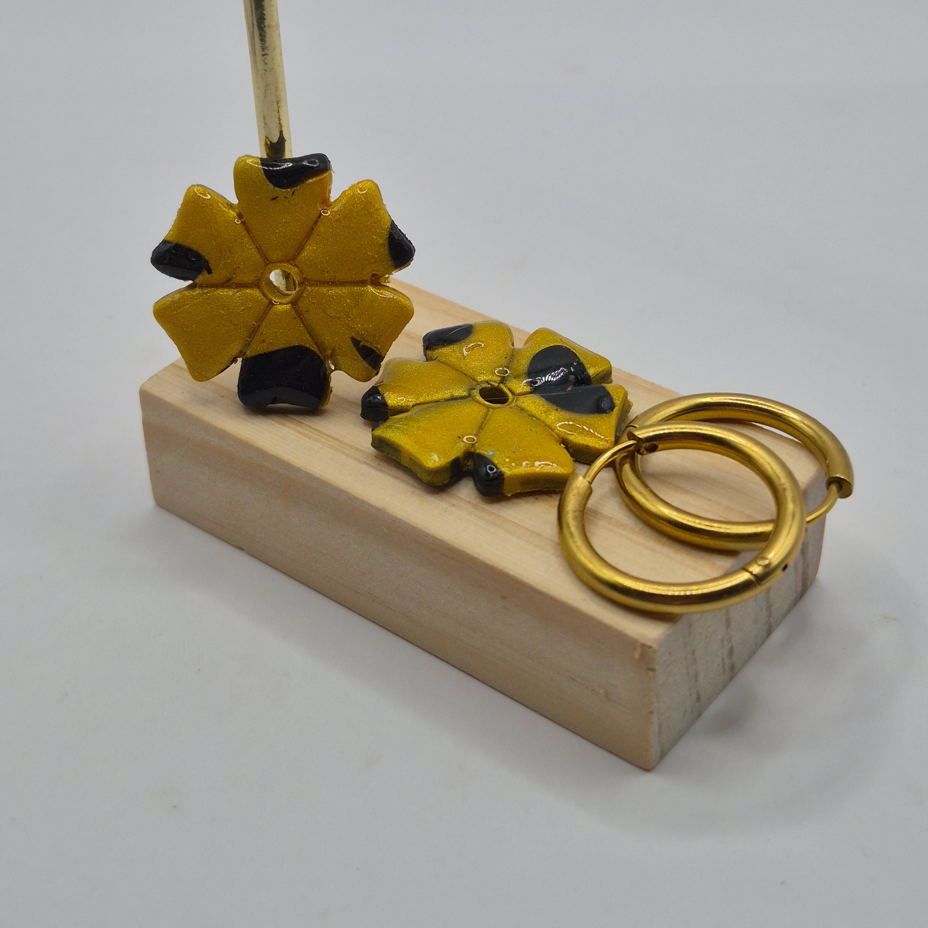 Parure Jessica : pampilles interchangeables en pâte polymère doré et noir, en forme de trèfle à 6 feuilles, présentées sur un support en bois, avec 2 créoles en acier inoxydable dorées.