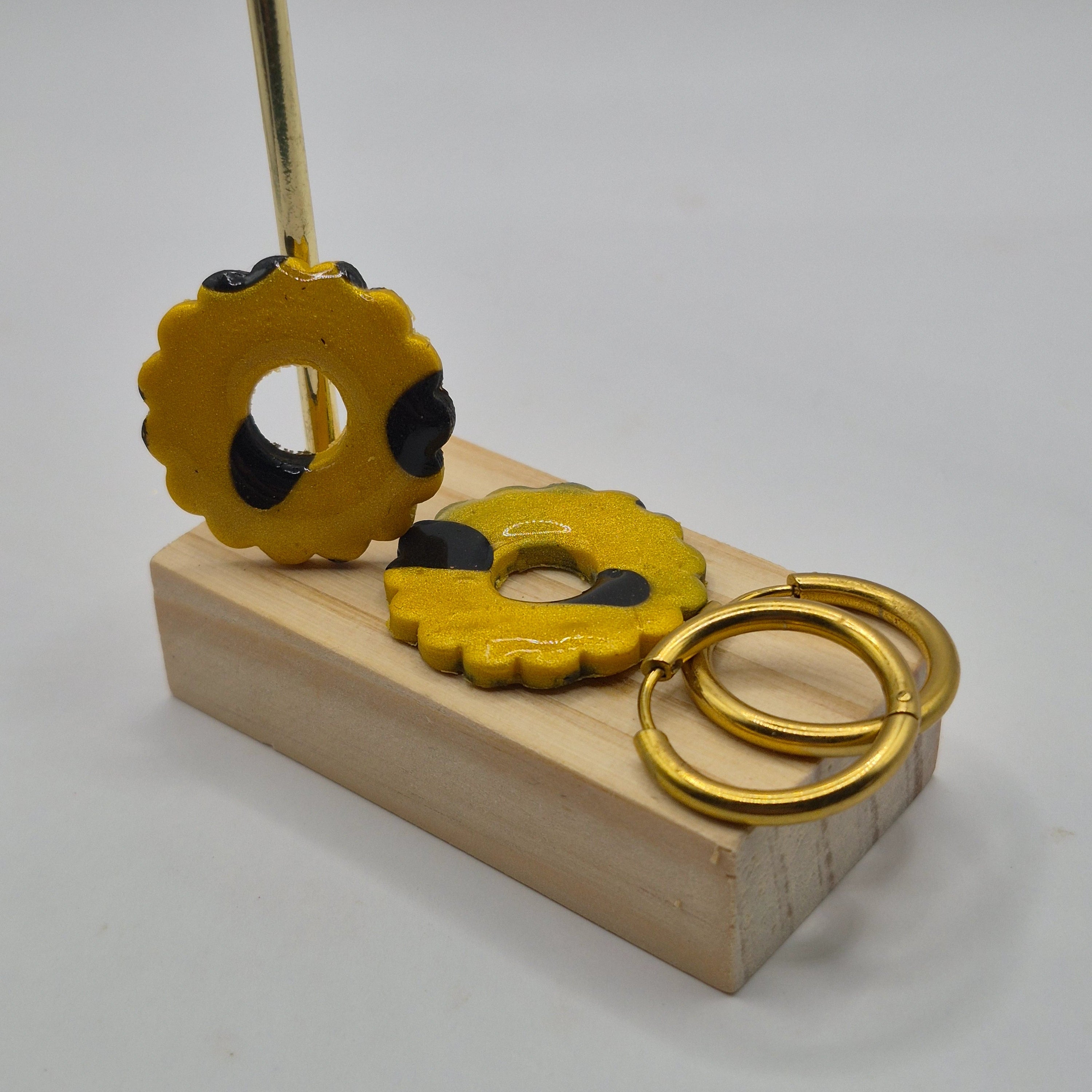 Parure Mélissa : pampilles interchangeables en pâte polymère noire et dorée pailletée, en forme de fleur, présentées sur un support en bois, avec 2 créoles en acier inoxydable dorées.