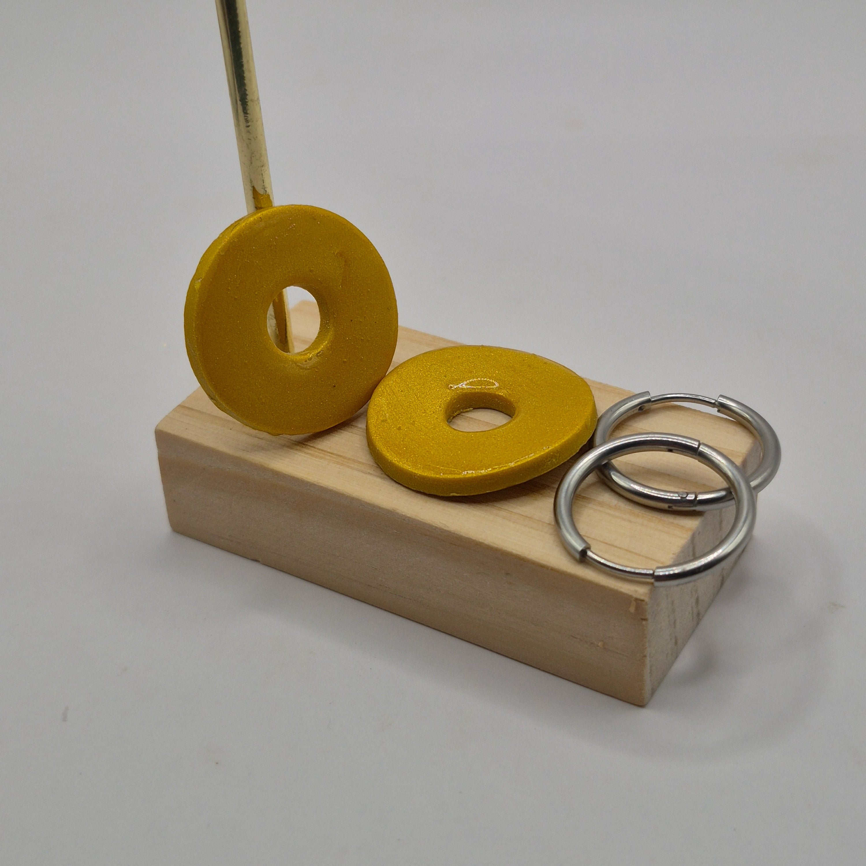 Parure Johanna: pampilles interchangeables en pâte polymère dorée, en forme de rond, présentées sur un support en bois, avec 2 créoles en acier inoxydable argentées.