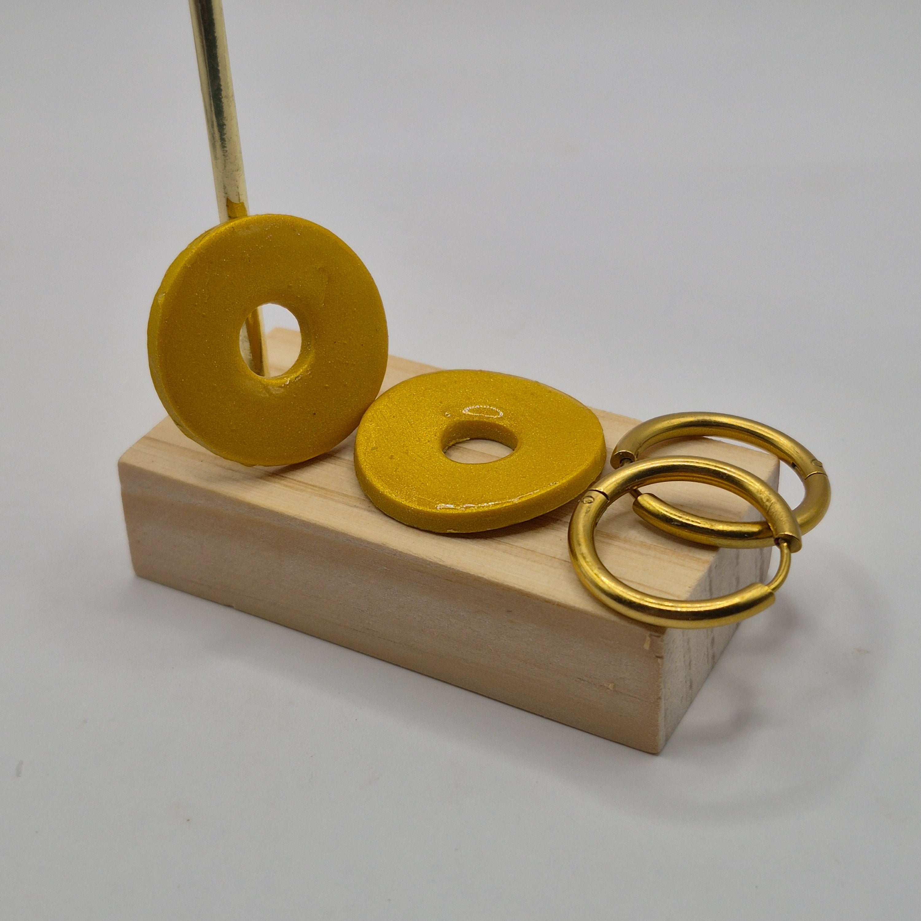 Parure Johanna : pampilles interchangeables en pâte polymère dorée, en forme de rond, présentées sur un support en bois, avec 2 créoles en acier inoxydable dorées.