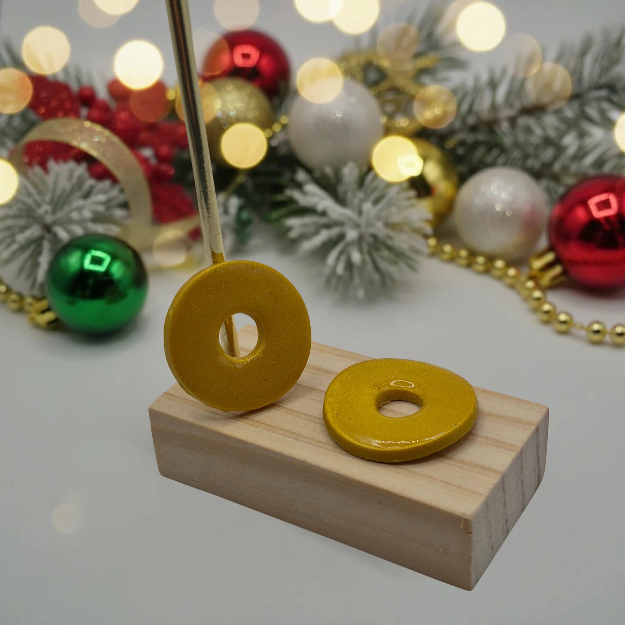 Parure  Johanna : pampilles interchangeables en pâte polymère dorée, en forme de rond, présentées sur un support en bois, et en arrière-plan des branches de sapin, des guirlandes et des boules de Noël.