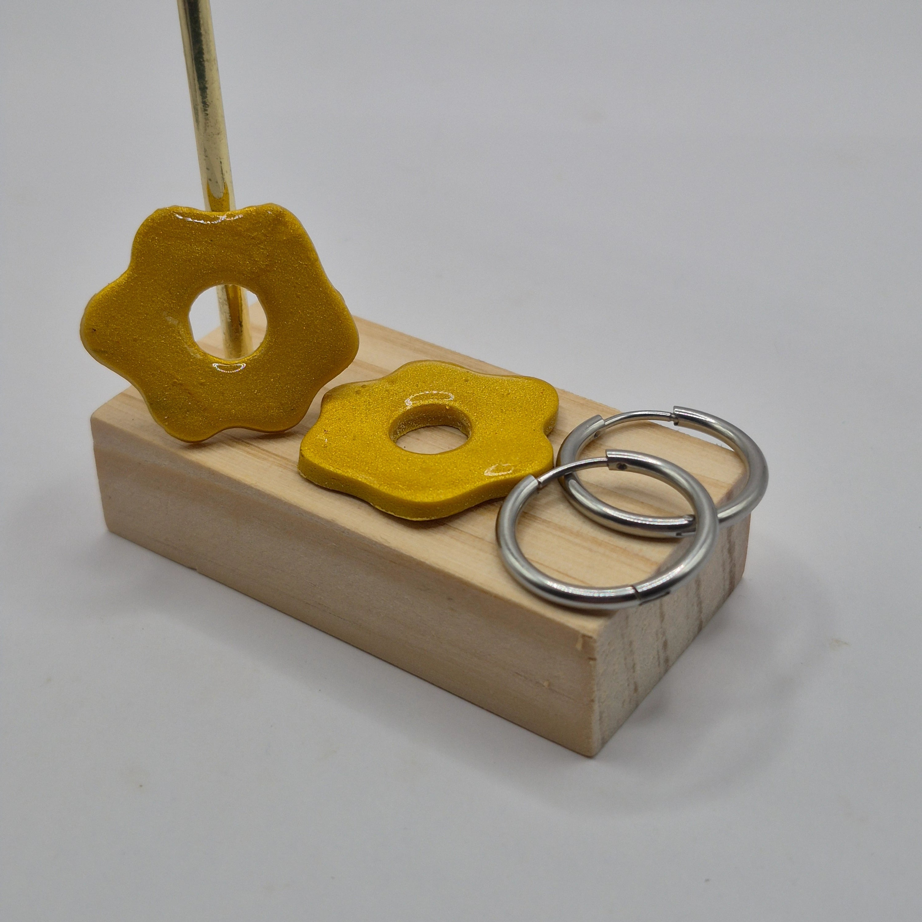 Parure Magalie : pampilles interchangeables en pâte polymère dorée et pailletée, en forme de fleur, présentées sur un support en bois, et deux créoles en acier inoxydable argentées.