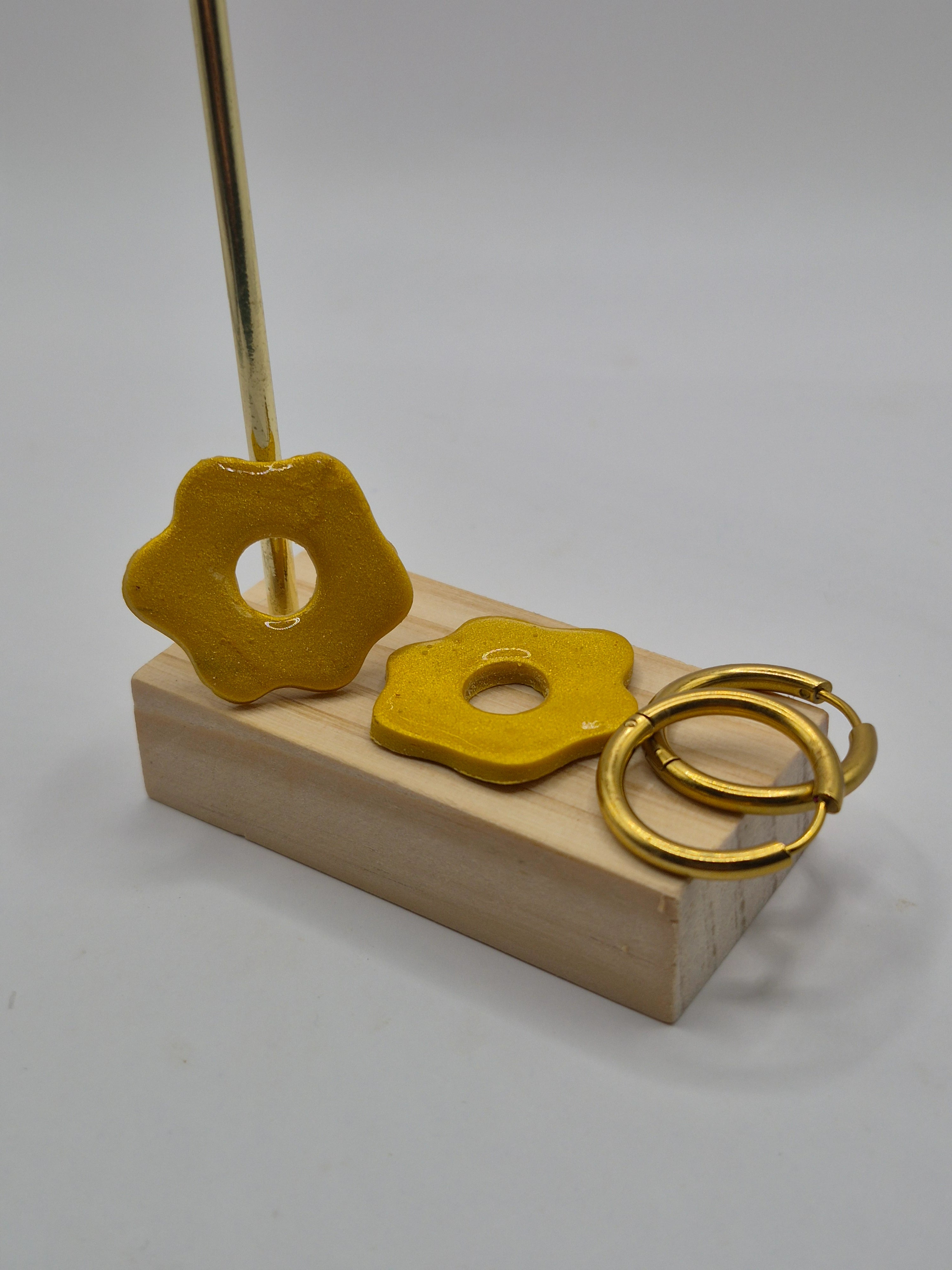 Parure Magalie : pampilles interchangeables en pâte polymère dorée et pailletée, en forme de fleur, présentées sur un support en bois, et deux créoles en acier inoxydable dorées.