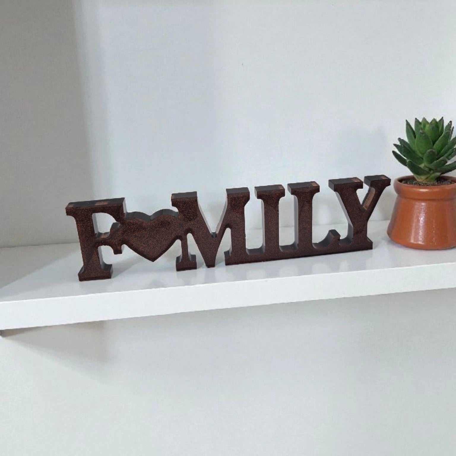 Décoration intérieure Family en résine pailletée cuivre posée sur étagère à côté d'une plante.