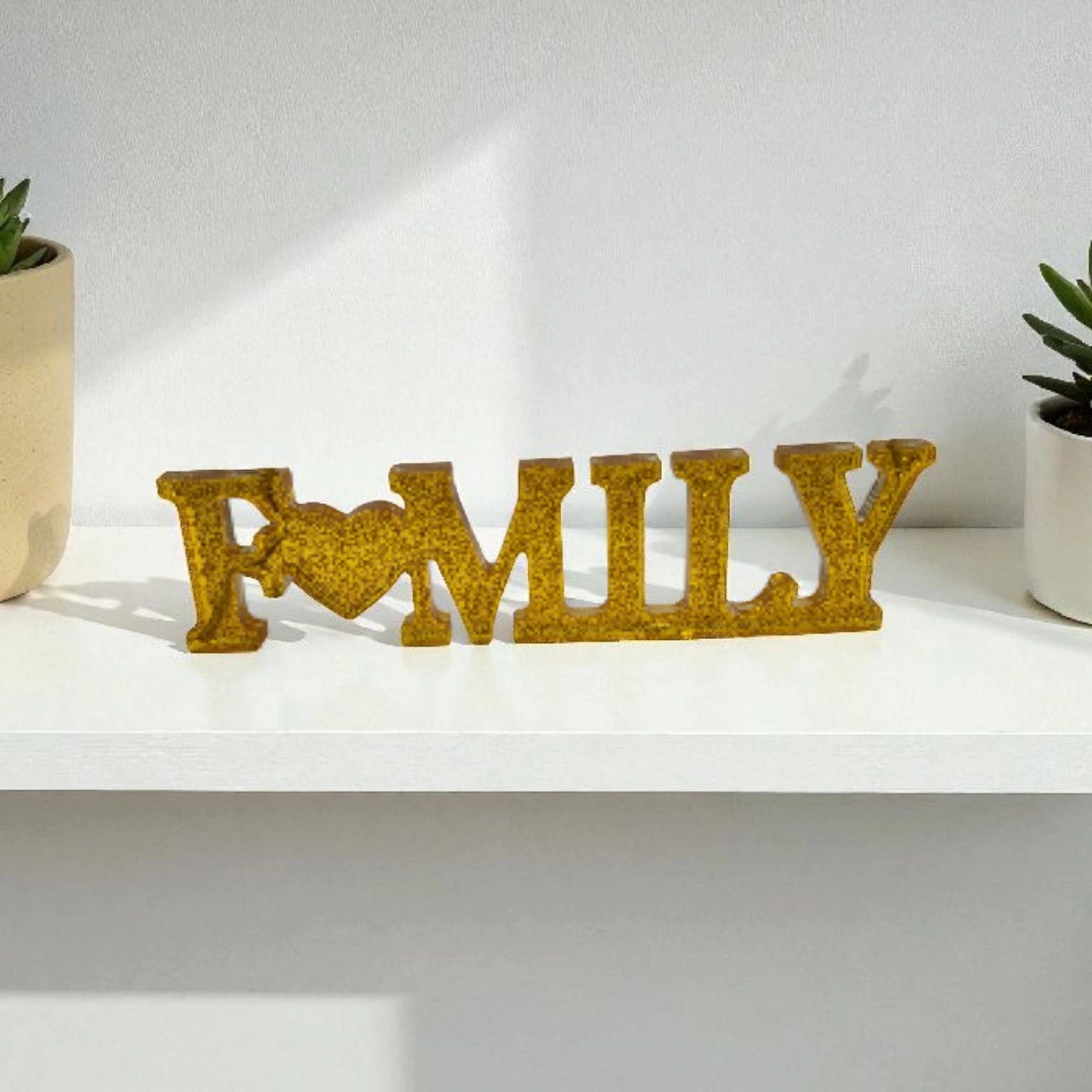 Décoration intérieure Family en résine pailletée doré posée sur étagère entre deux plantes