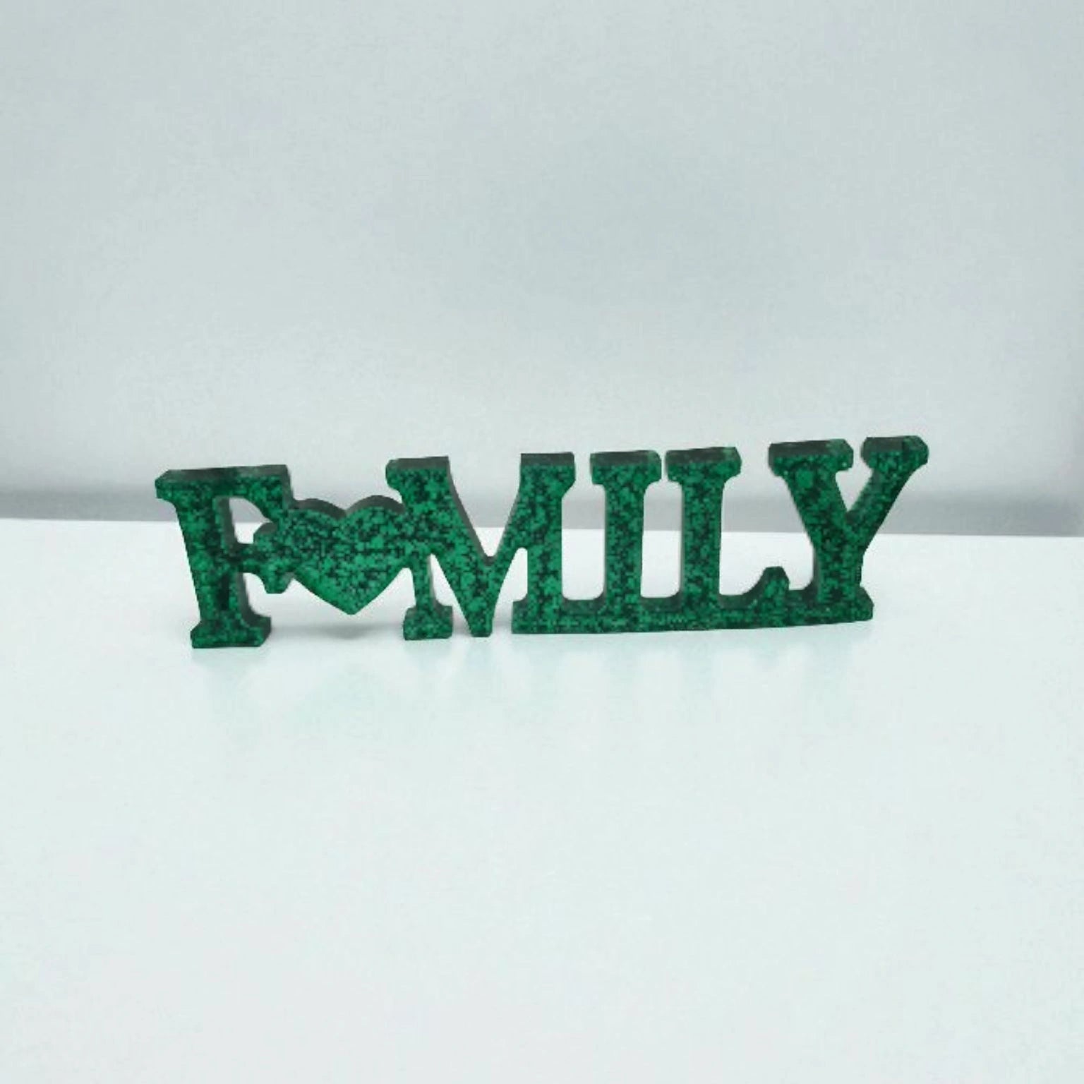 Décoration intérieure Family en résine pailletée verte posée sur surface plane neutre