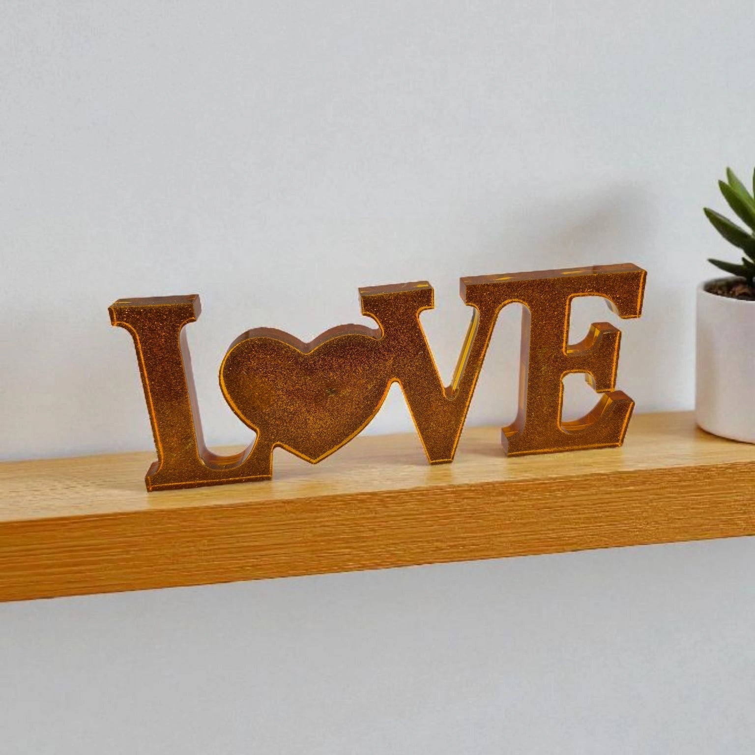 Décoration intérieure avec inscription Love en résine pailletée de couleur or, posée sur une étagère à côté d'une plante verte