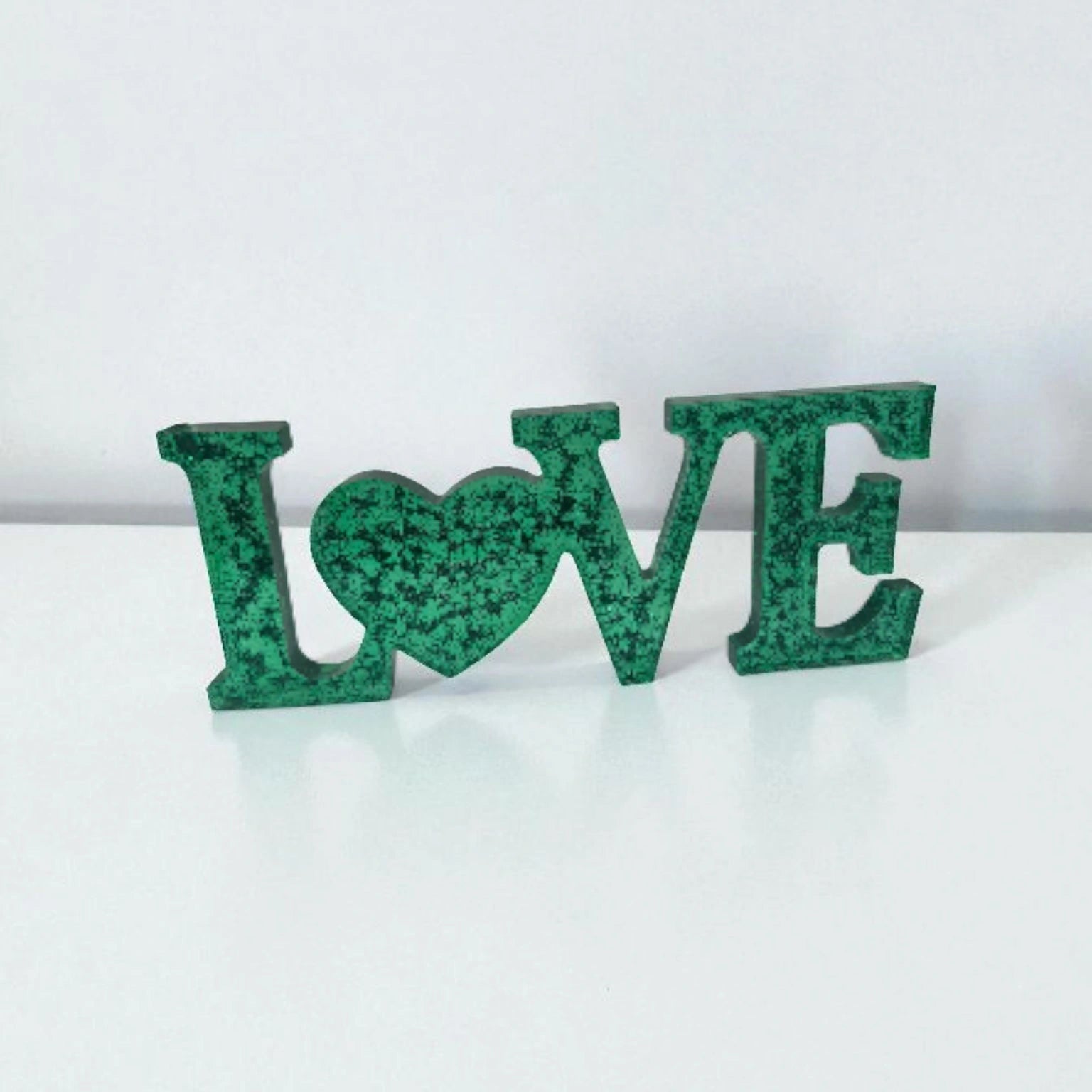 Décoration intérieure avec inscription Love en résine pailletée de couleur or, posée sur une surface neutre.