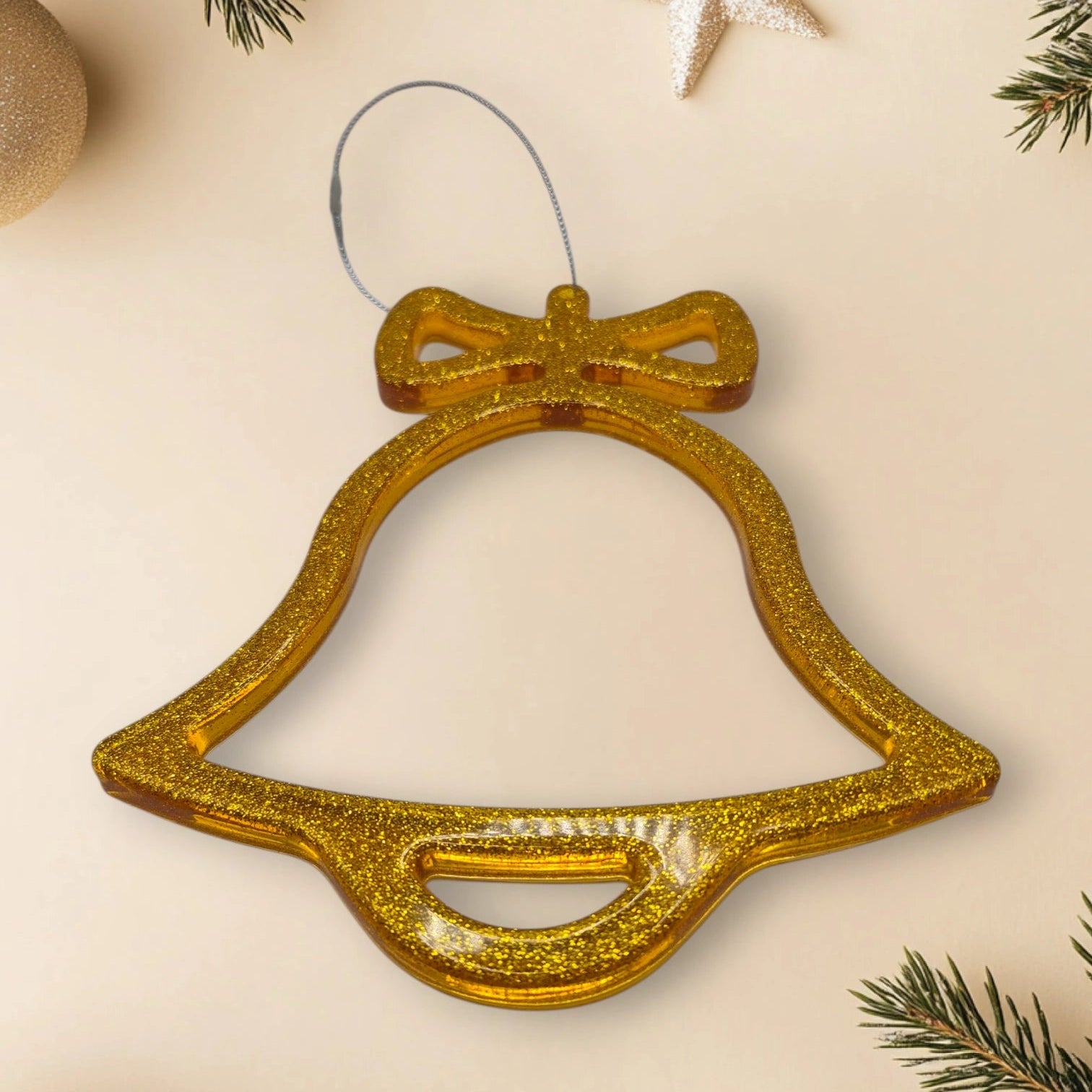 suspension de noël en forme de cloche en résine pailletée dorée posée sur un fond décoratif avec branche de sapin et étoiles scintillantes