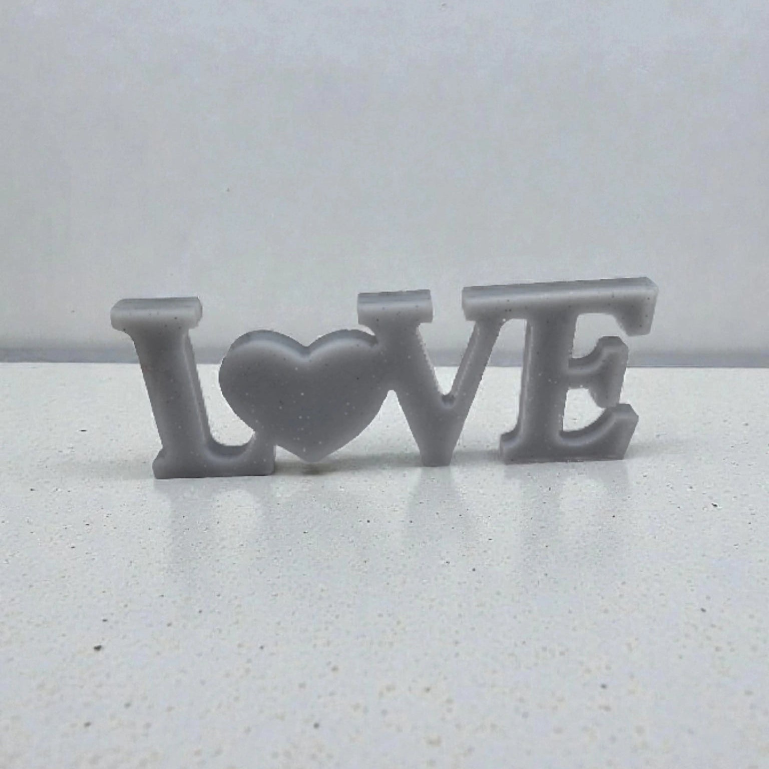 Décoration intérieure avec inscription Love en résine pailletée de couleur argent, posée sur une surface neutre.