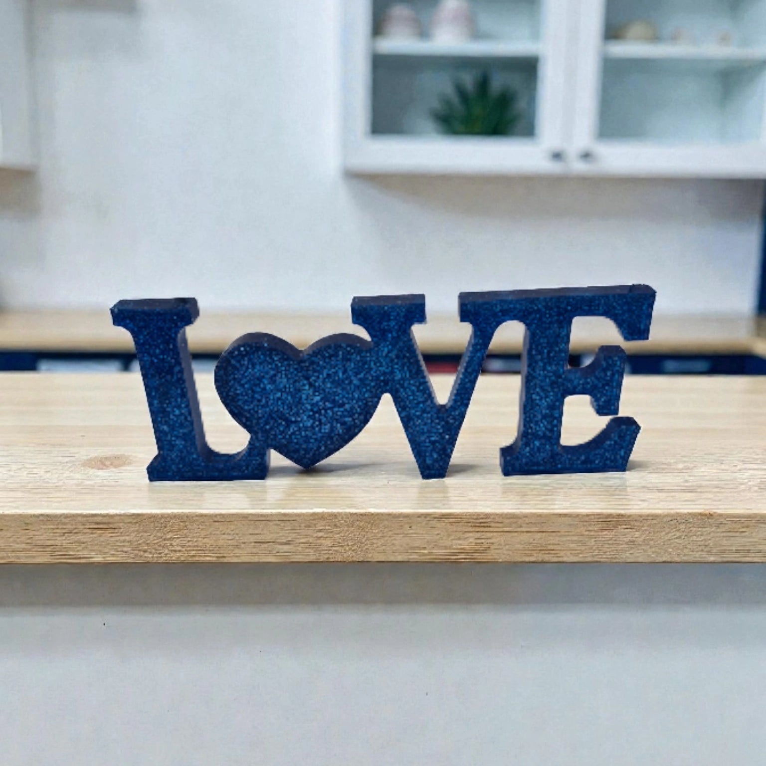 Décoration intérieure avec inscription Love en résine pailletée de couleur bleue, posée sur une surface neutre.