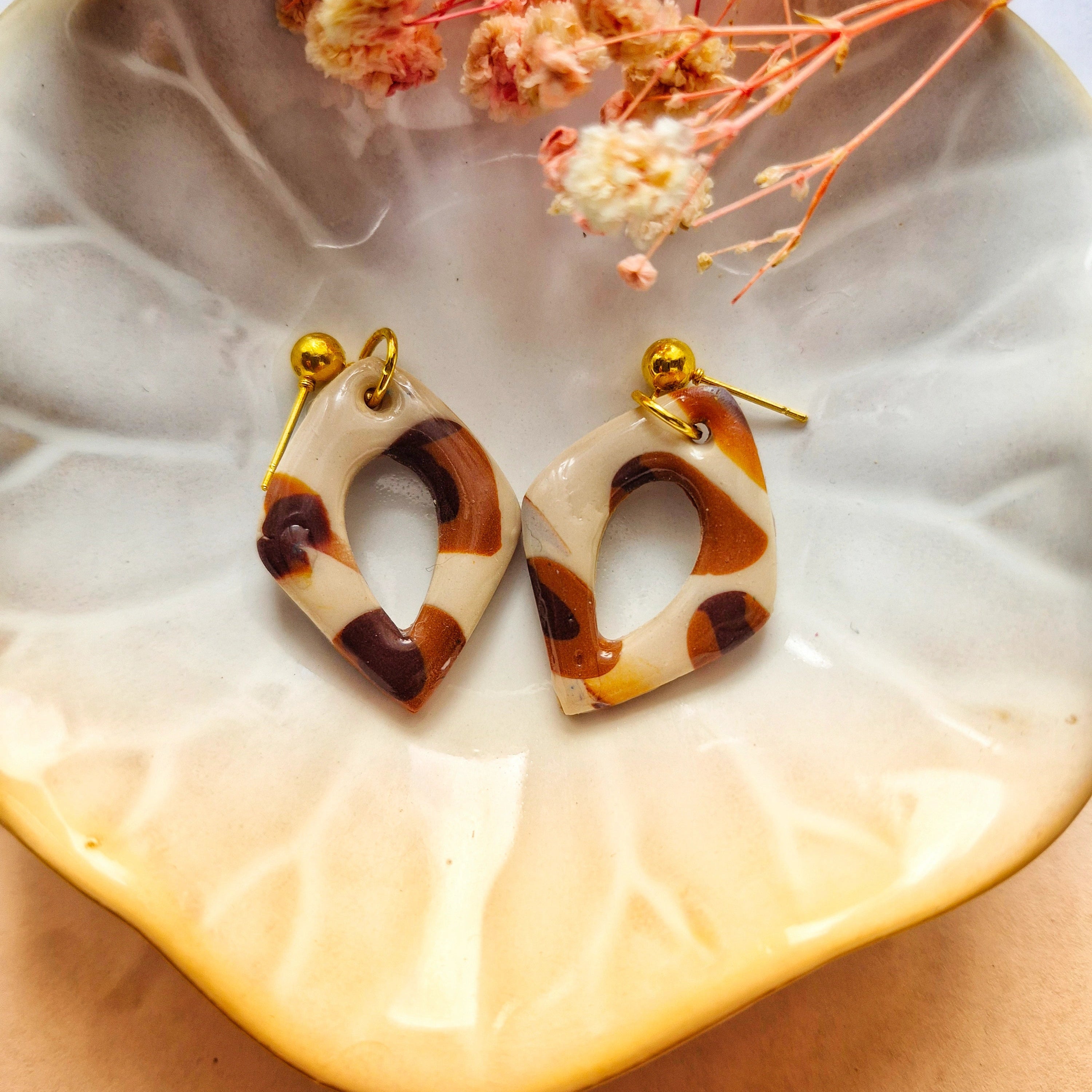Photo d'une pampille, modèle Marcia au motif léopard (couleur marron). Pampilles avec clous d'oreilles de couleur or, disposées dans une assiette. Accessoire vendu par les Créa de Marlène