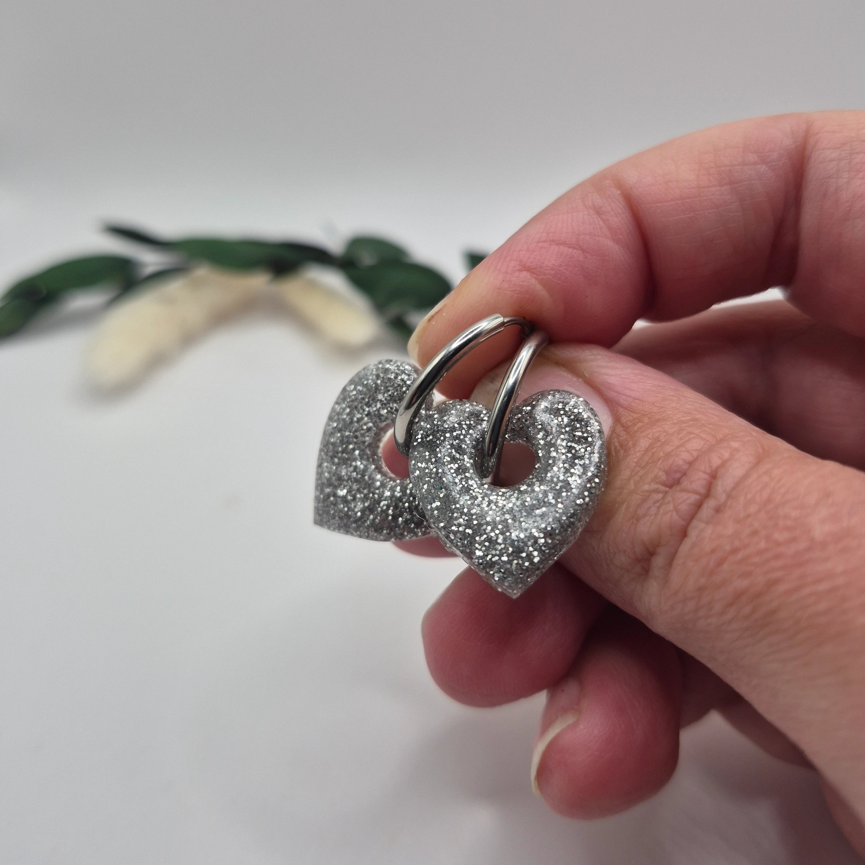 Pampilles Coralie argentées résine pailletée sur créoles inoxydables  argentées tenues à la main avec branche verte et pampa en fond de décor