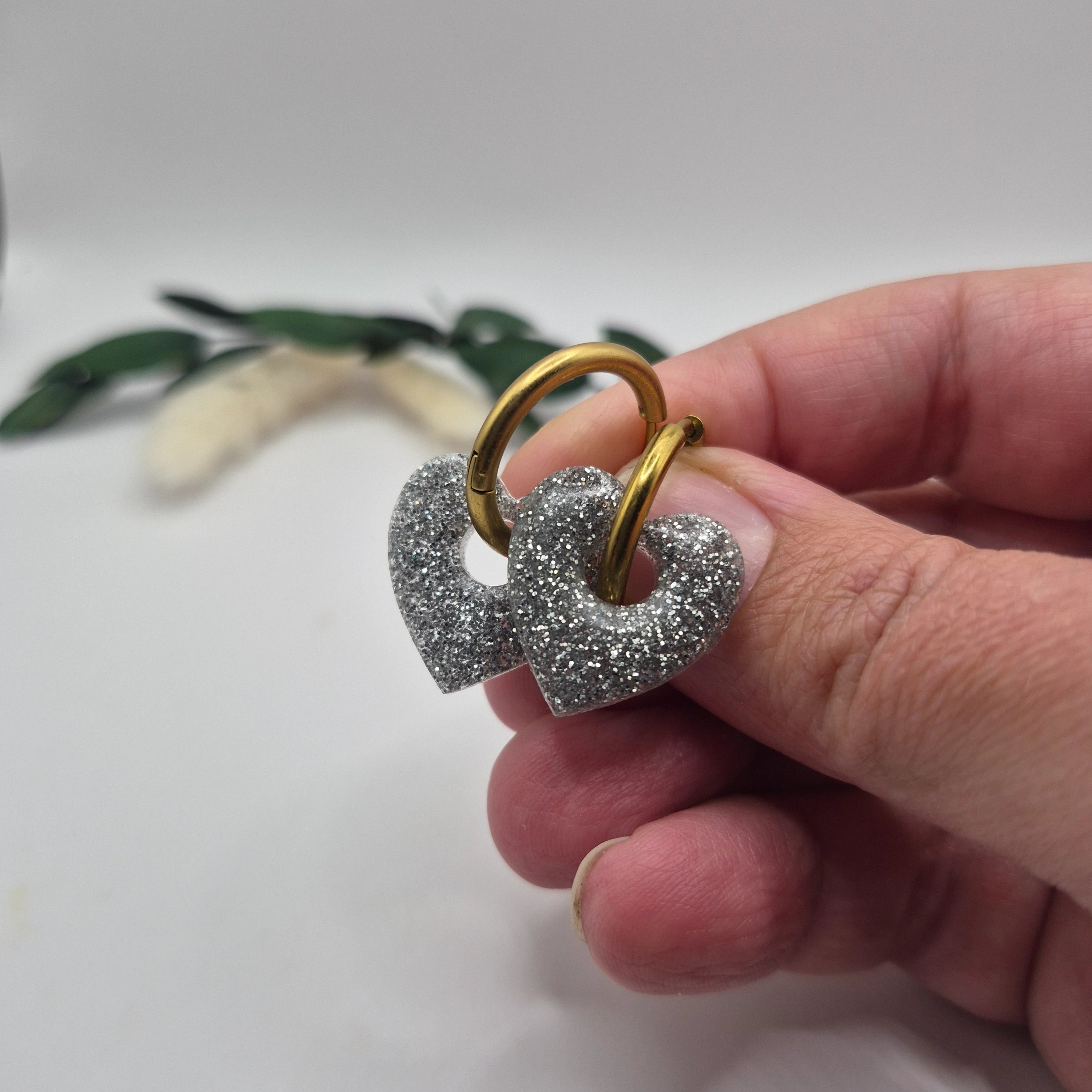 Pampilles Coralie argentées résine pailletée sur créoles inoxydables  dorées tenues à la main avec branche verte et pampa en fond de décor