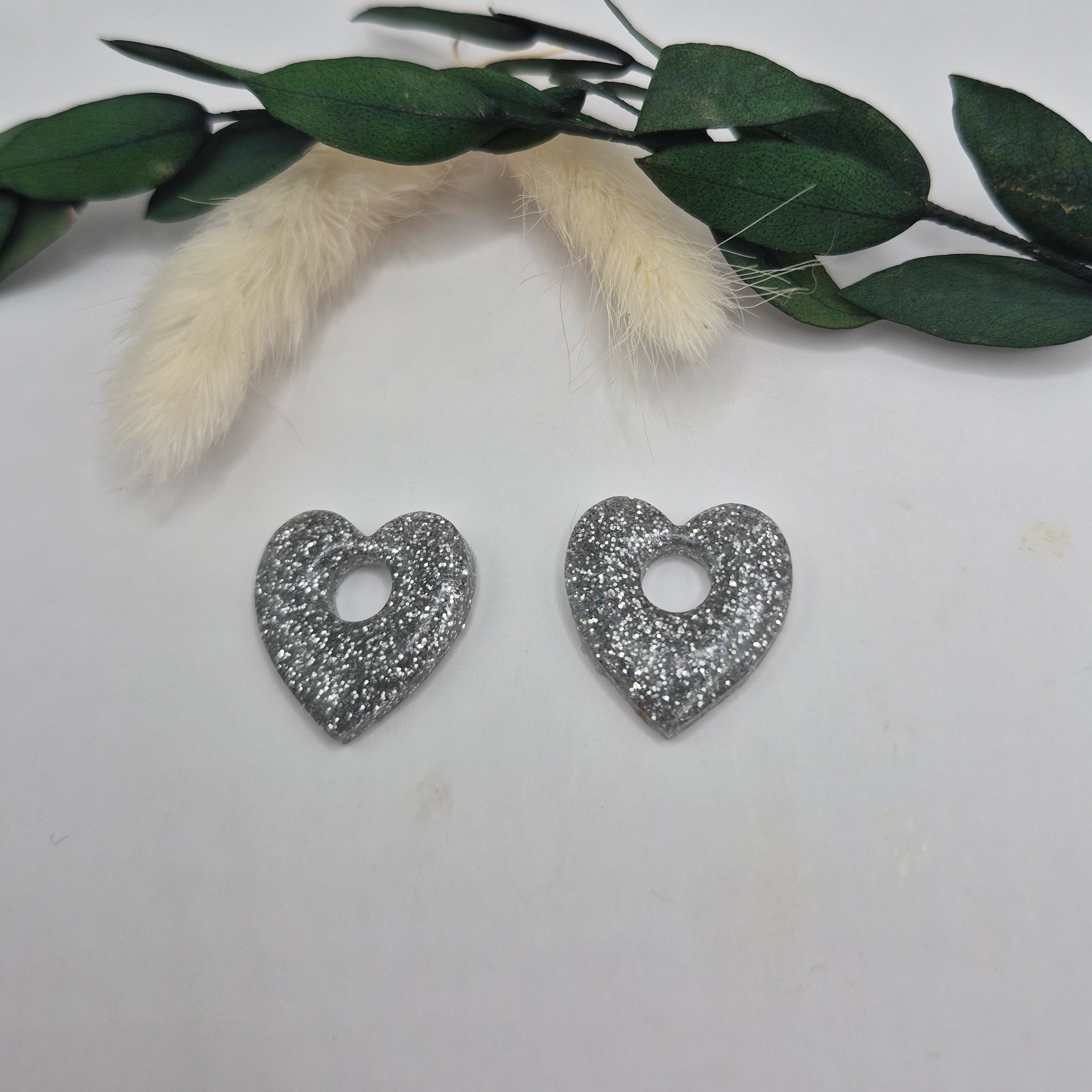 Pampilles Coralie argentées résine pailletée posées à plat avec branche verte et pampa en fond de décor