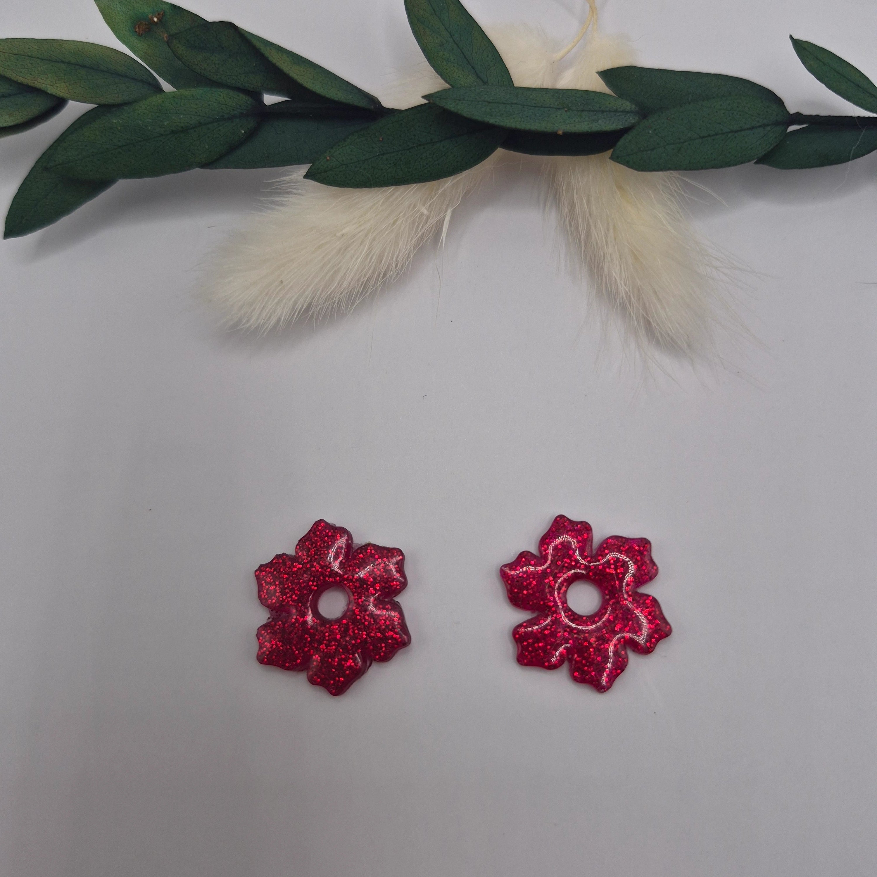 Boucles d’oreilles pampilles rouges Elodie en résine époxy pailletée posées à plat sur fond neutre avec branche de pampa et feuilles