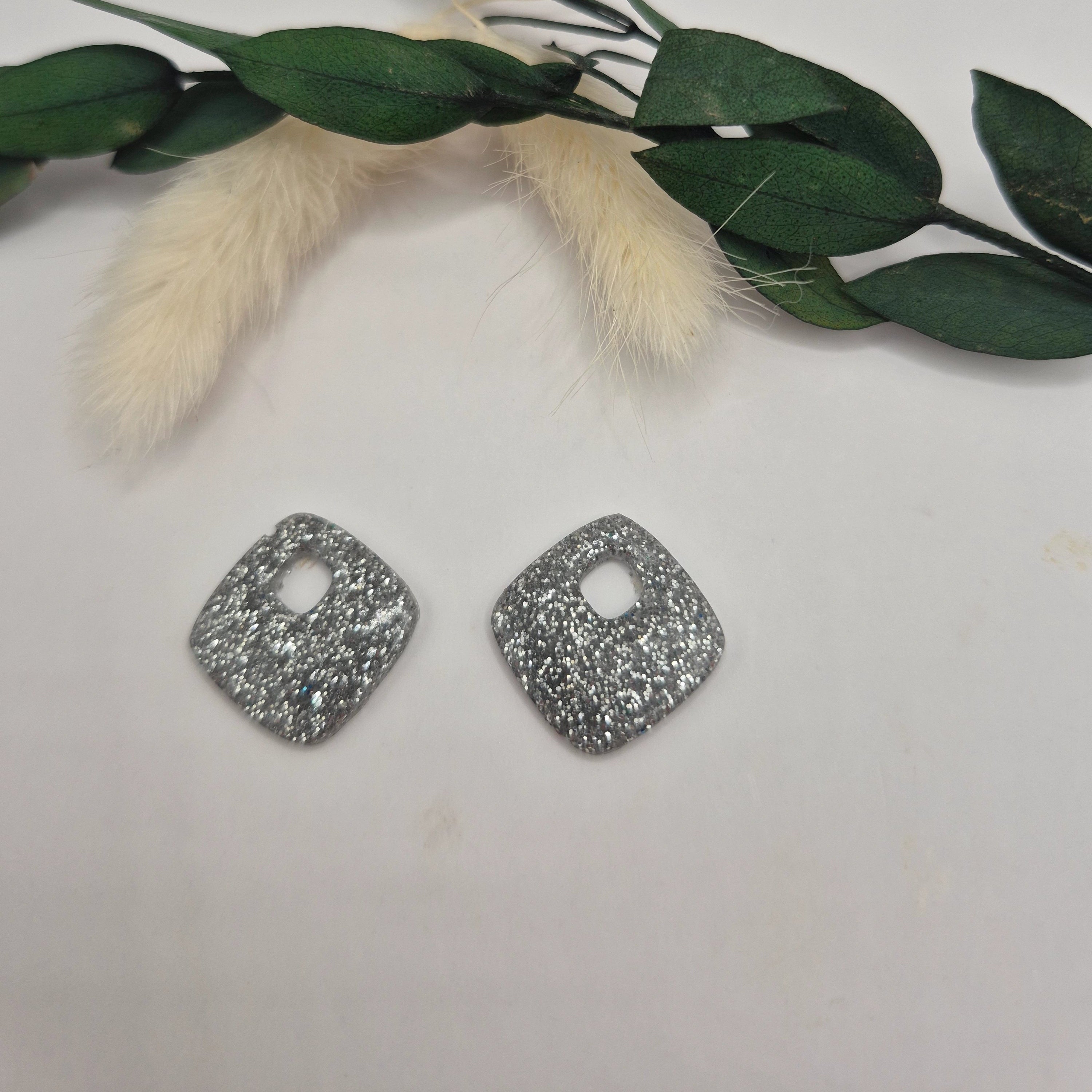 Pampilles Millie losange argent en résine avec créoles inoxydables couleur argent, posées à plat sur surface neutre, décor pampa et feuilles vertes