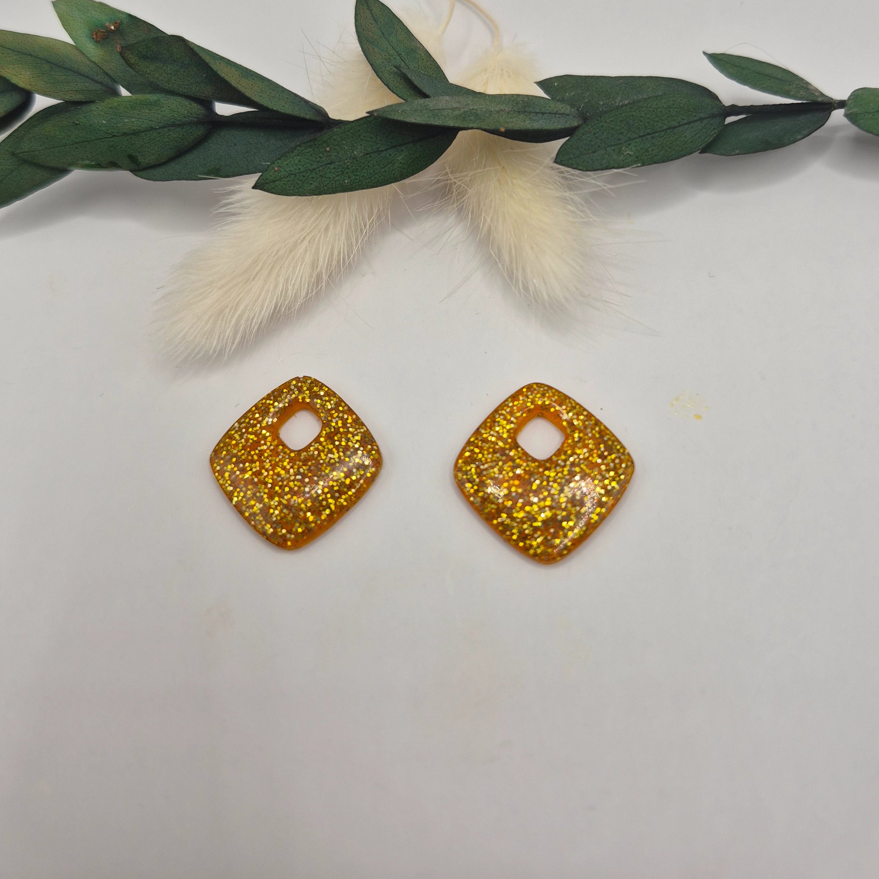 Pampilles Millie losange bleues en résine , main tenant les boucles d'oreilles, décor pampa et feuilles vertes