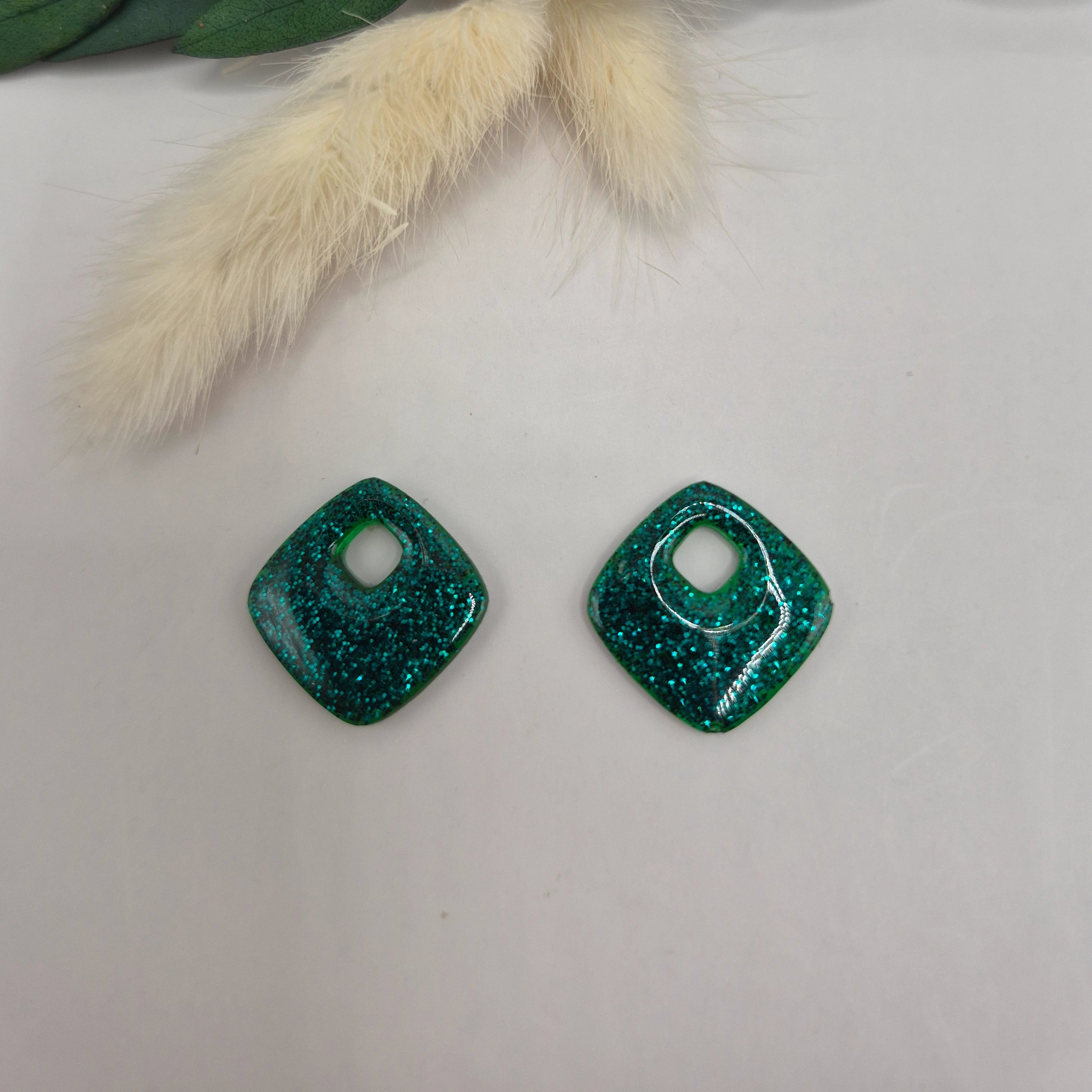 Pampilles Millie losange argent en résine posées à plat sur surface neutre, décor pampa et feuilles vertes