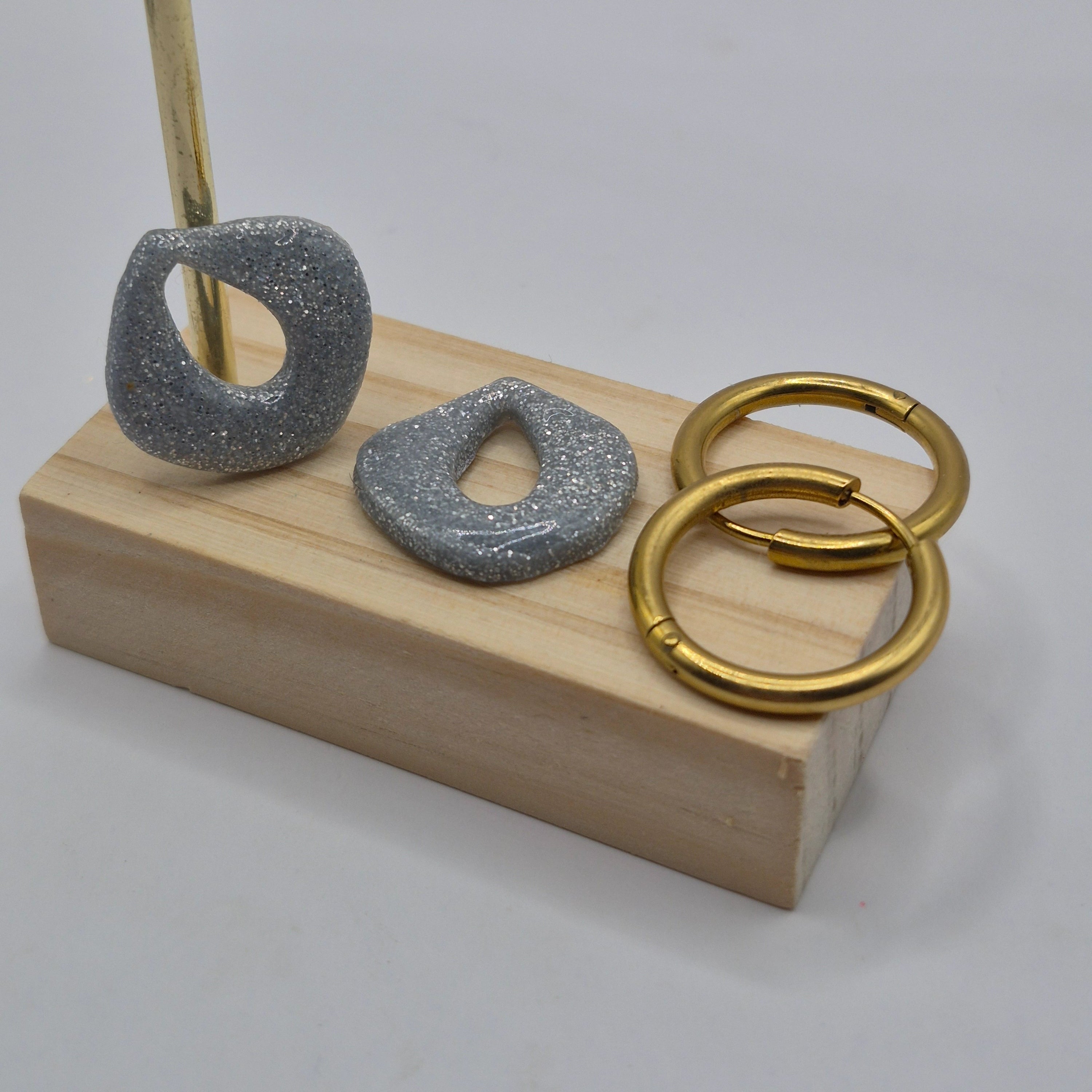 Parure Cynthia : pampilles interchangeables en pâte polymère gris argenté pailletée, en forme de goutte d'eau, présentées sur un support en bois, avec deux créoles en acier inoxydables dorées.