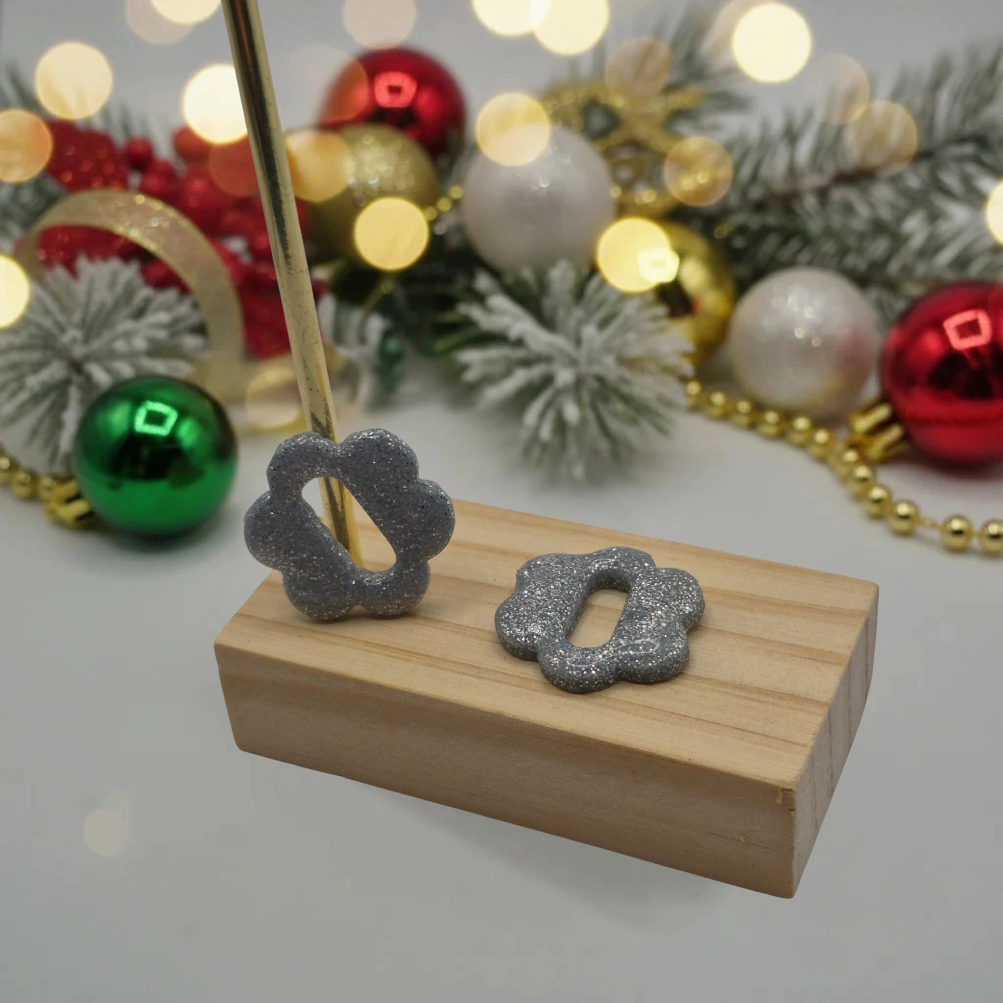 Parure Sophie : pampilles interchangeables en pâte polymère argentée pailletée, en forme de fleur nuage, présentées sur un support en bois, et en arrière-plan des branches de sapin, des guirlandes et des boules de Noël.