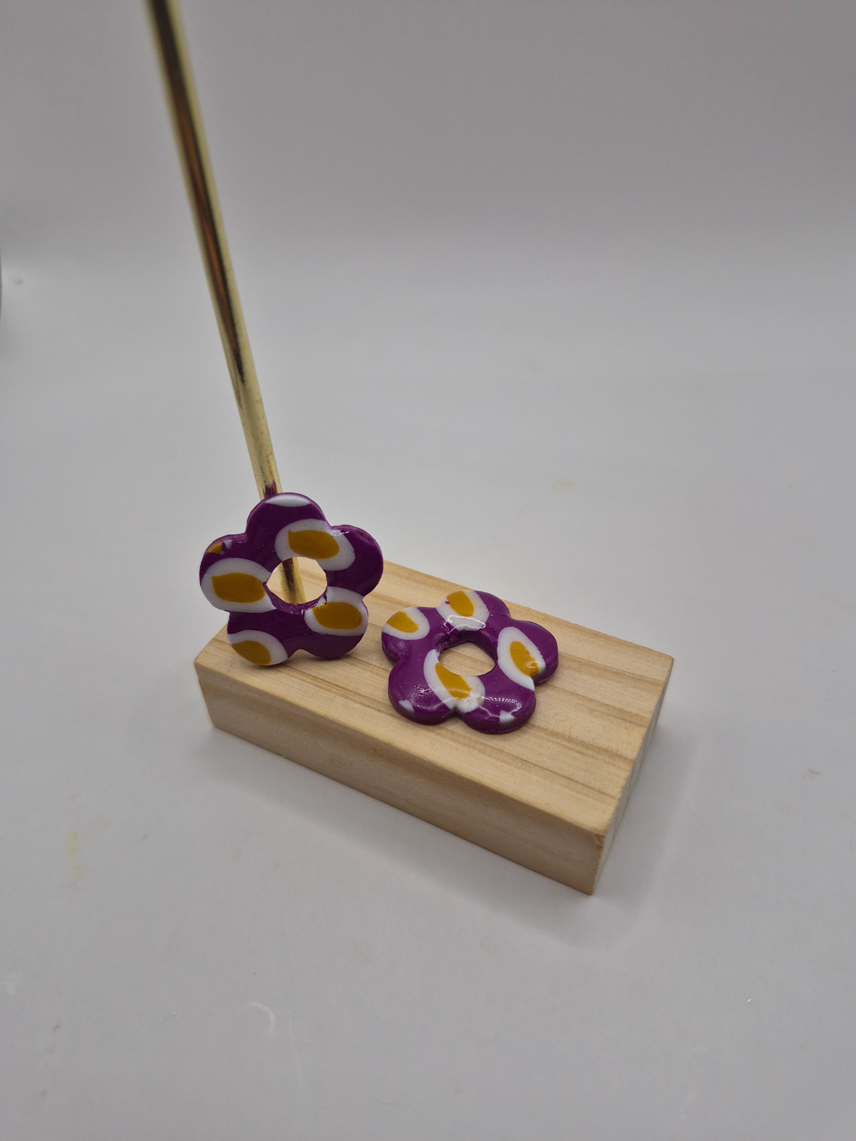 Pampilles fleur violet avec motif rond blanc et ocre en pâte polymère pour boucles d’oreilles interchangeables – accessoires créatifs faits main pour bijoux artisanaux, présentés sur un support en bois.