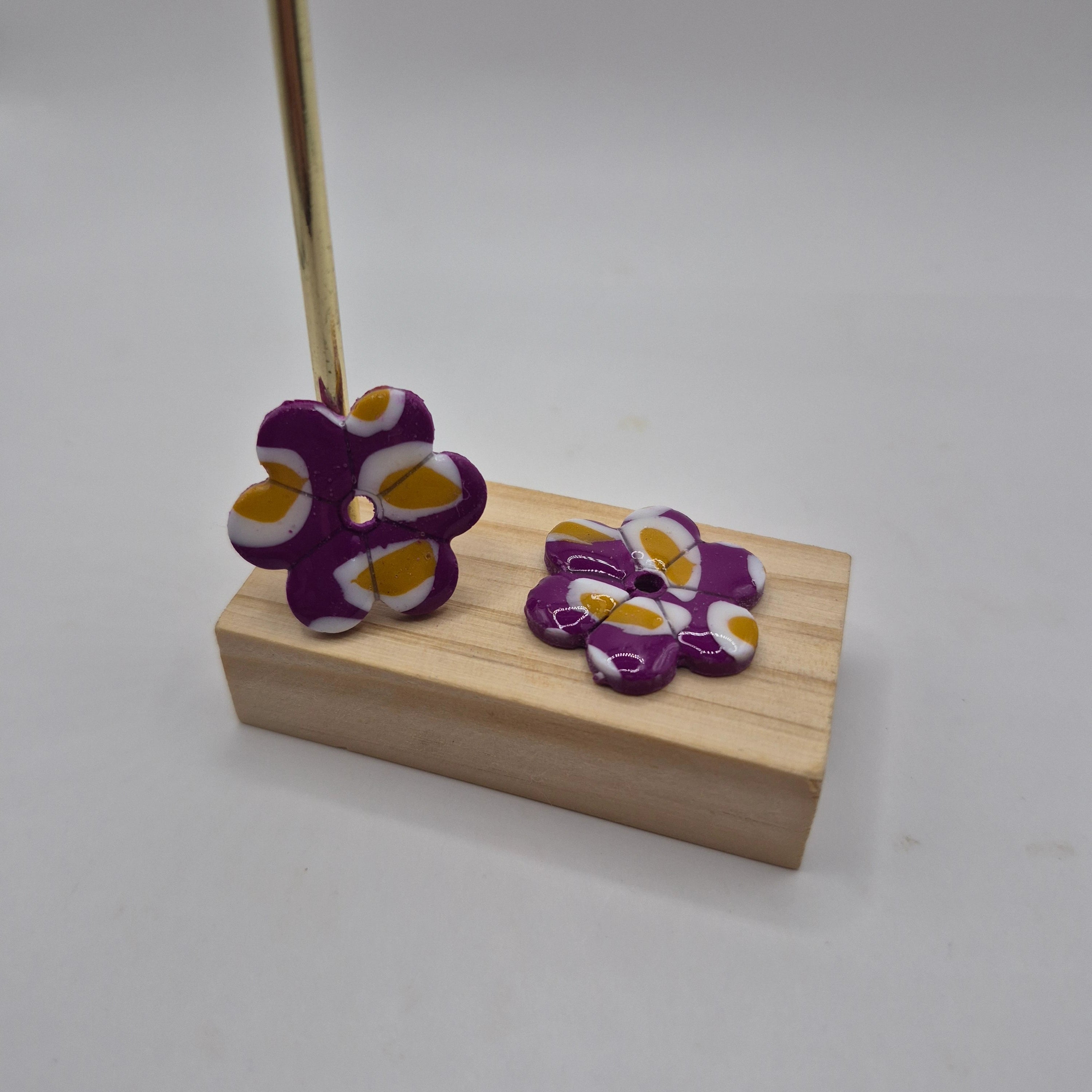 Boucles d’oreilles pampilles fleur en pâte polymère violet, blanc et ocre faites main, finition résine présentées sur un support en bois  — parure Lilia artisanale.