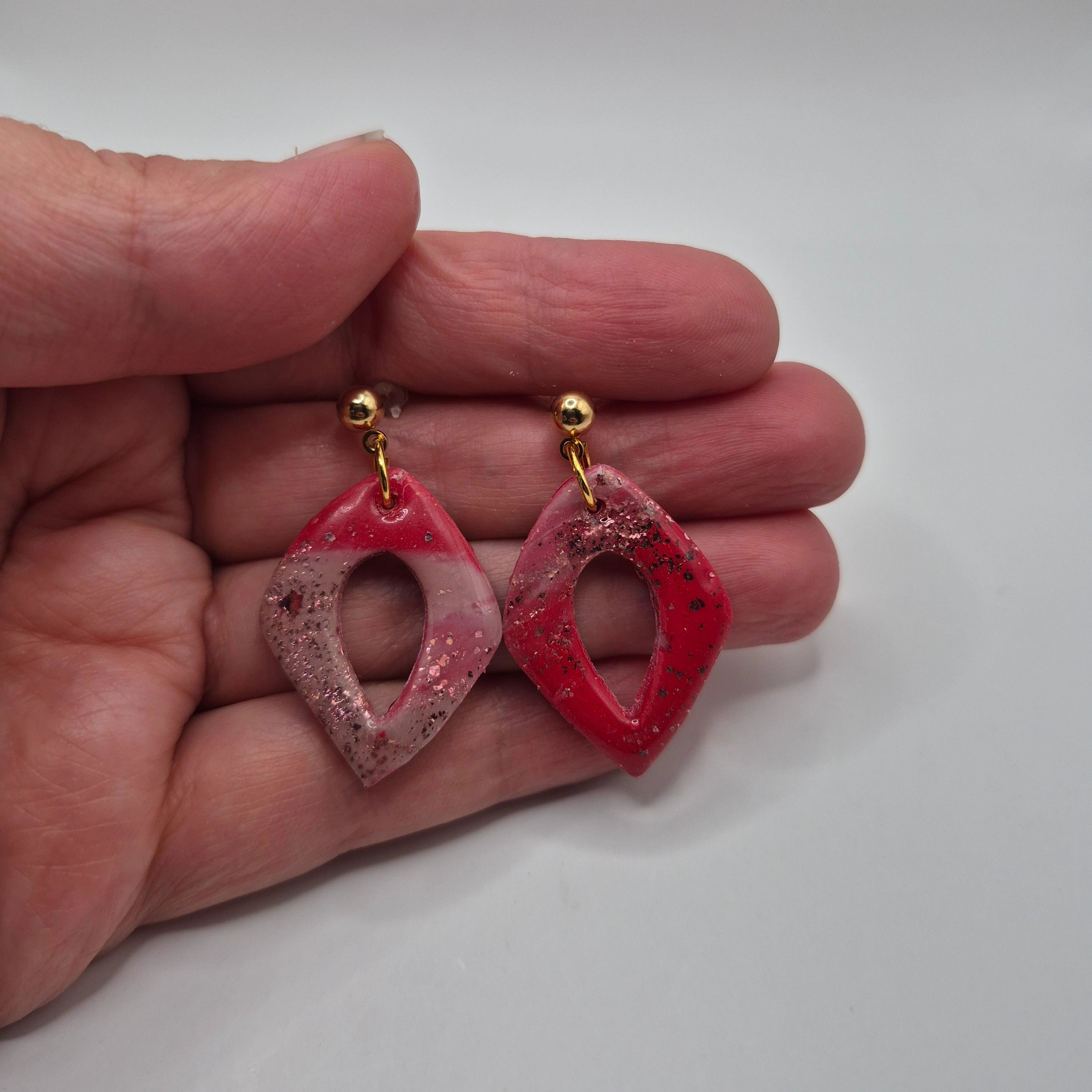 Boucle d'oreilles ou Pampilles Marcia en pâte polymère rose, finition résine, de forme losange, avec attaches à clous en acier inoxydable doré, présentées à la main.