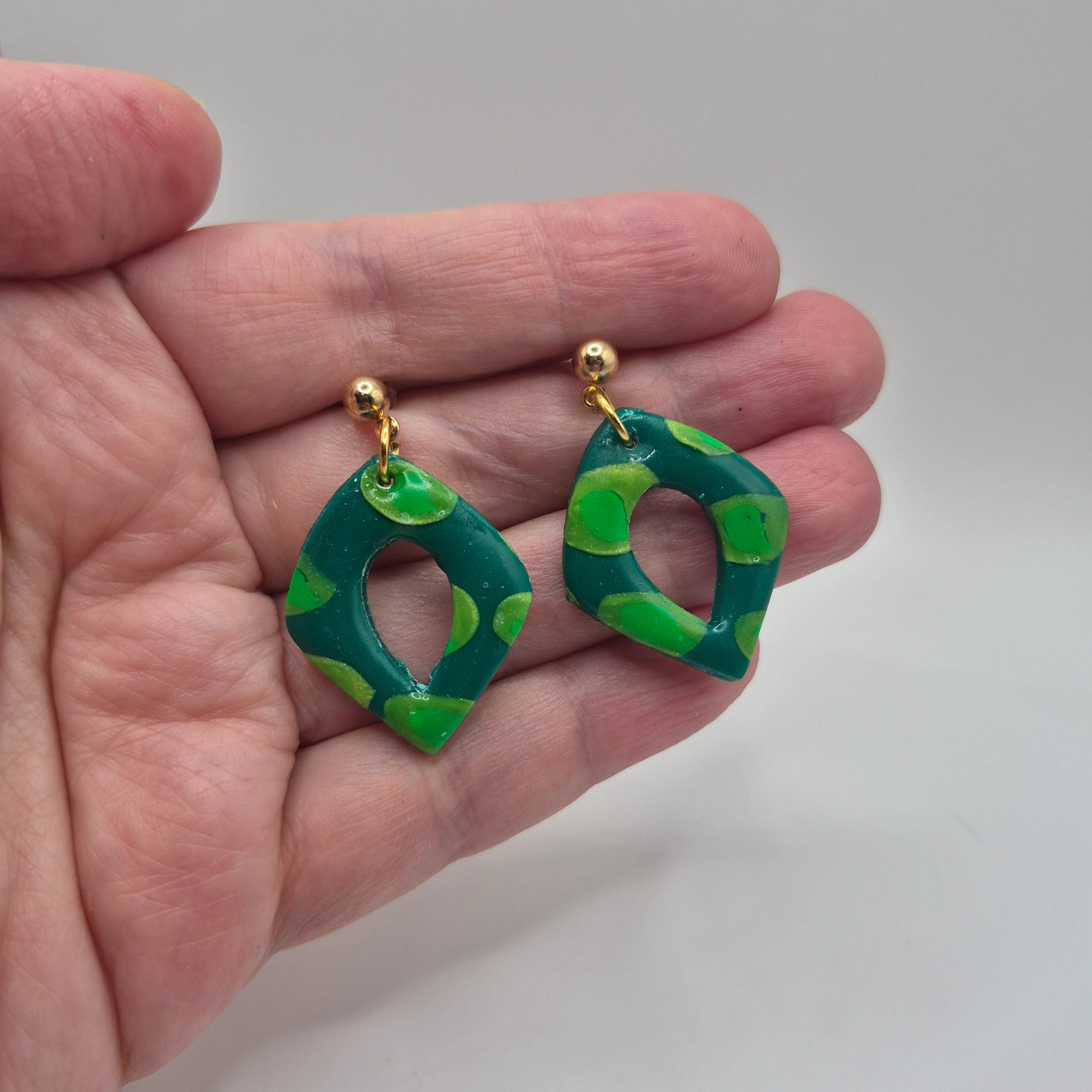 Boucle d'oreilles ou Pampilles Marcia en pâte polymère verte, finition résine, de forme losange, avec attaches à clous en acier inoxydable doré, présentées à la main.