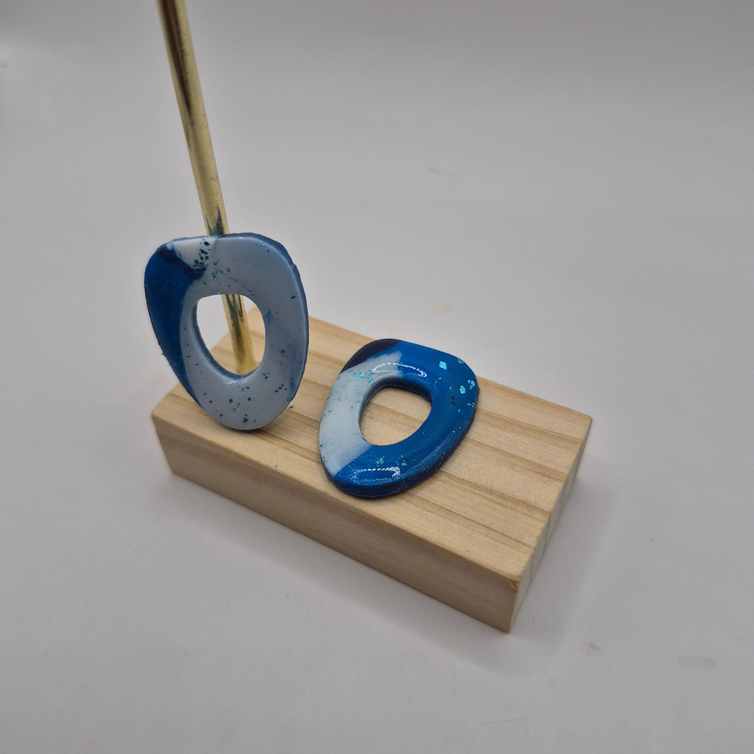 Boucles d’oreilles pampilles en pâte polymère bleu et blanc, de forme arrondie et géométrique, présentées sur un support en bois — parure Mia.