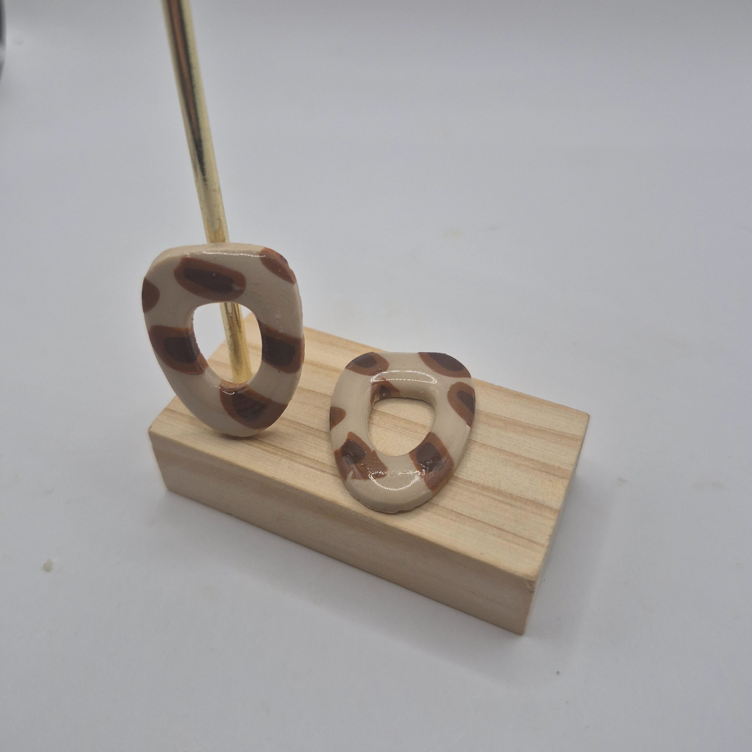 Boucles d’oreilles pampilles en pâte polymère motif léopard, de forme arrondie et géométrique, présentées sur un support en bois — parure Mia.