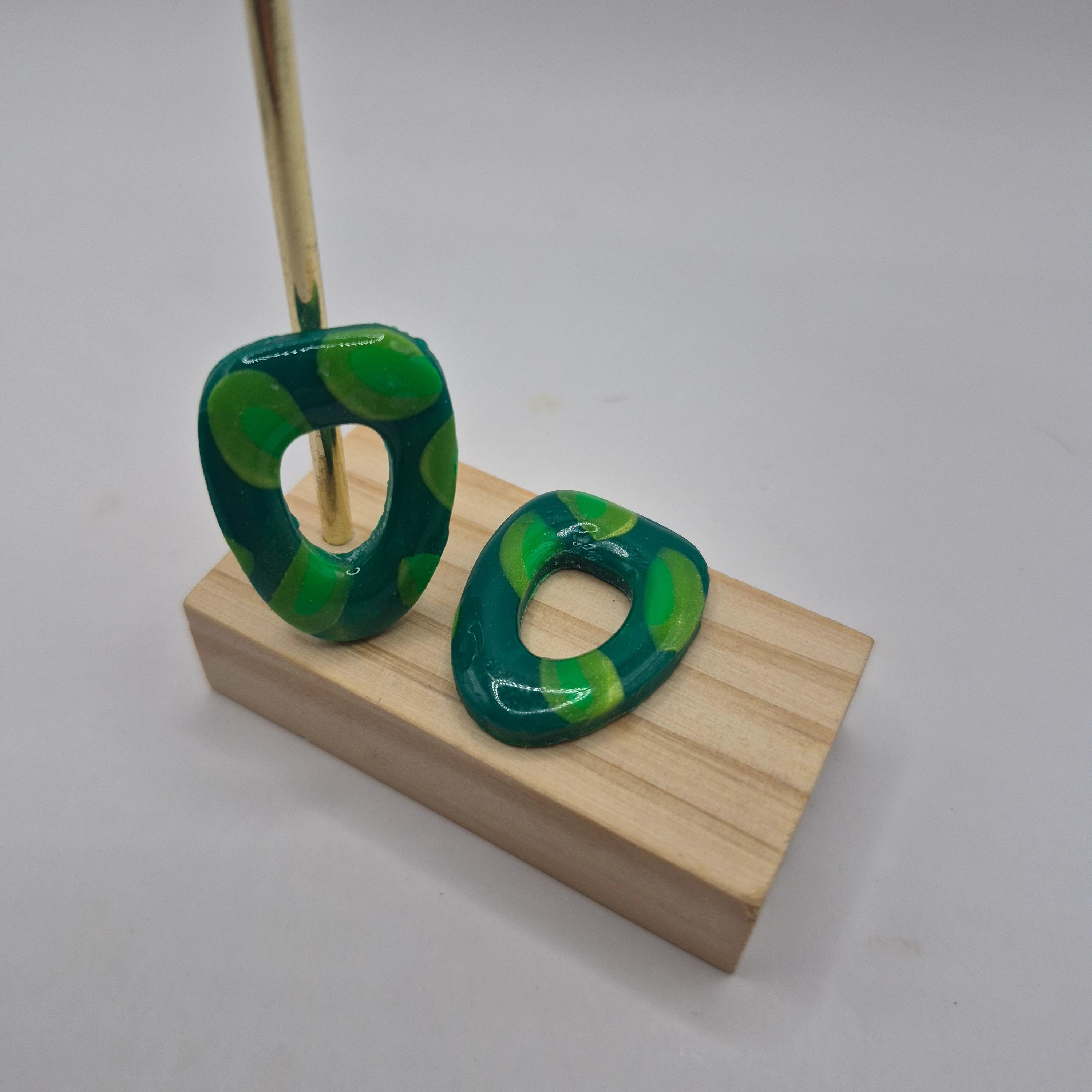 Boucles d’oreilles pampilles en pâte polymère vert, de forme arrondie et géométrique, présentées sur un support en bois — parure Mia.