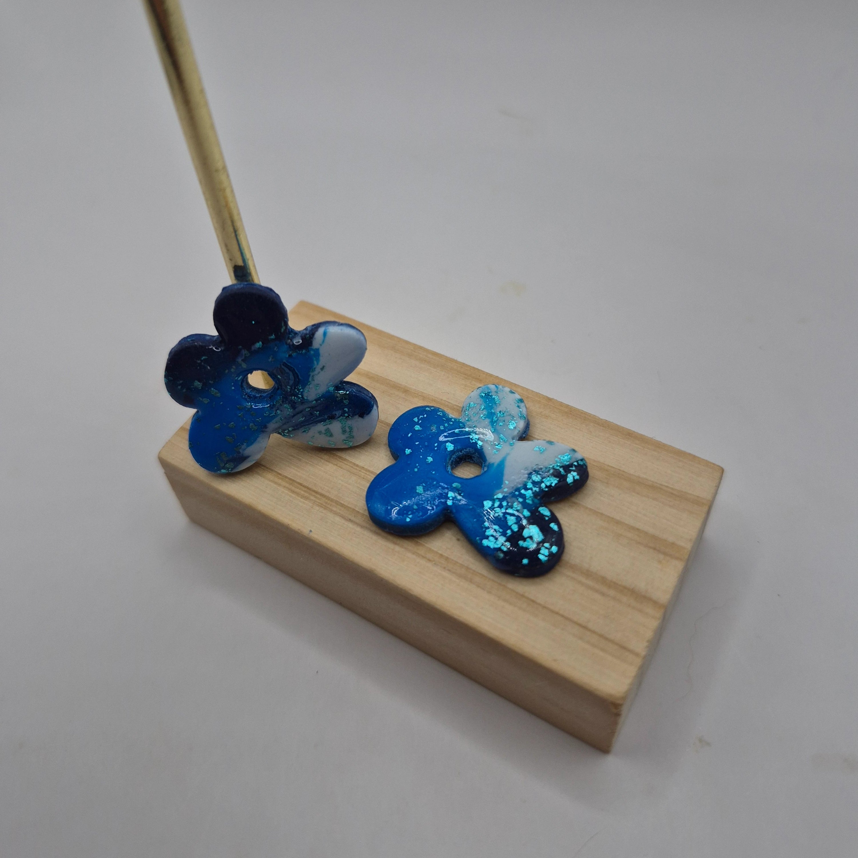 Boucles d’oreilles pampilles fleur difforme en pâte polymère bleu et blanc pailletée faites main, finition résine présentées sur un support en bois — parure Noelia artisanale