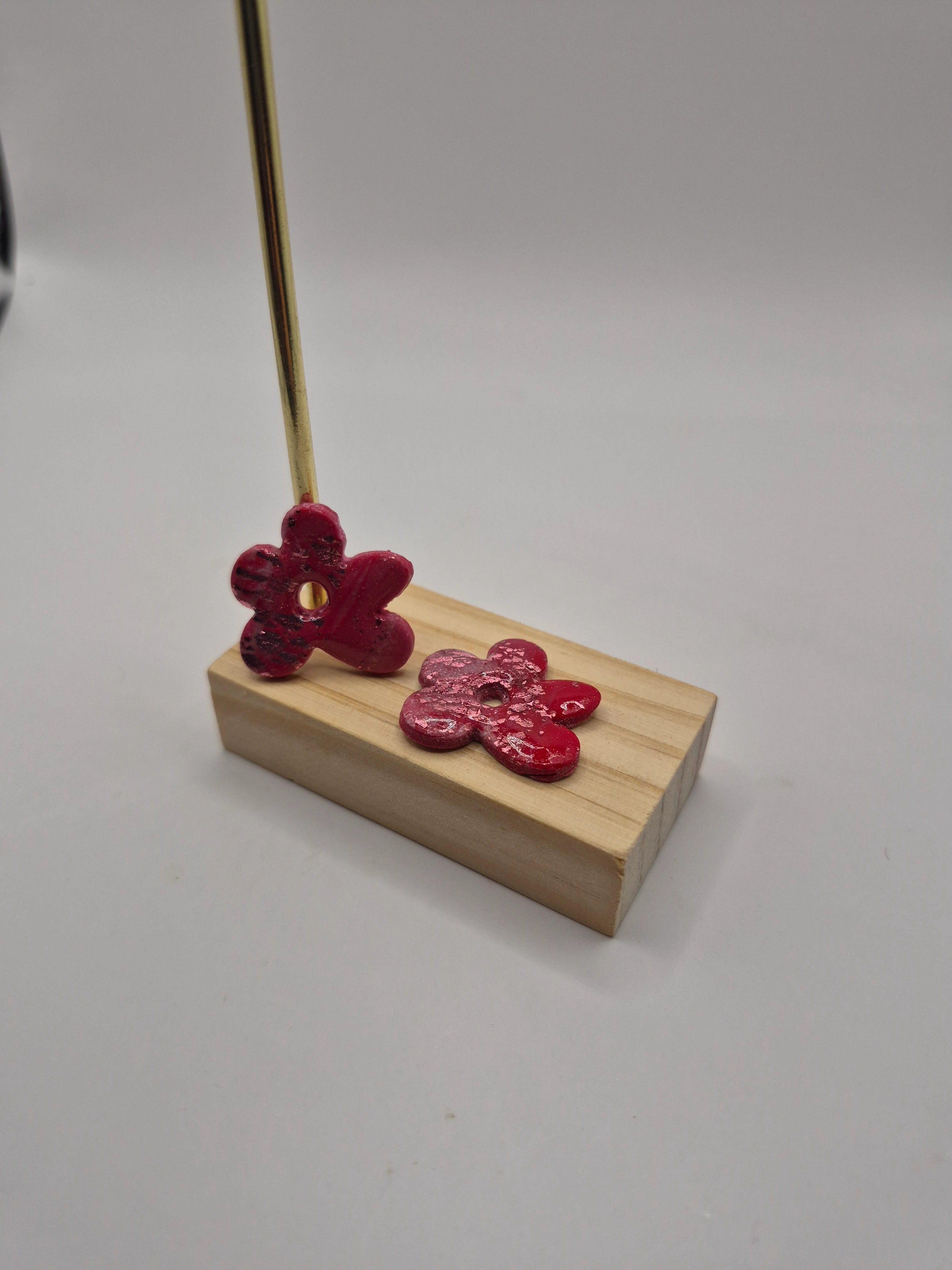Boucles d’oreilles pampilles en forme de fleur irrégulière, en pâte polymère  rose, faites main avec finition résine, présentées sur un support en bois  — parure artisanale Noelia.