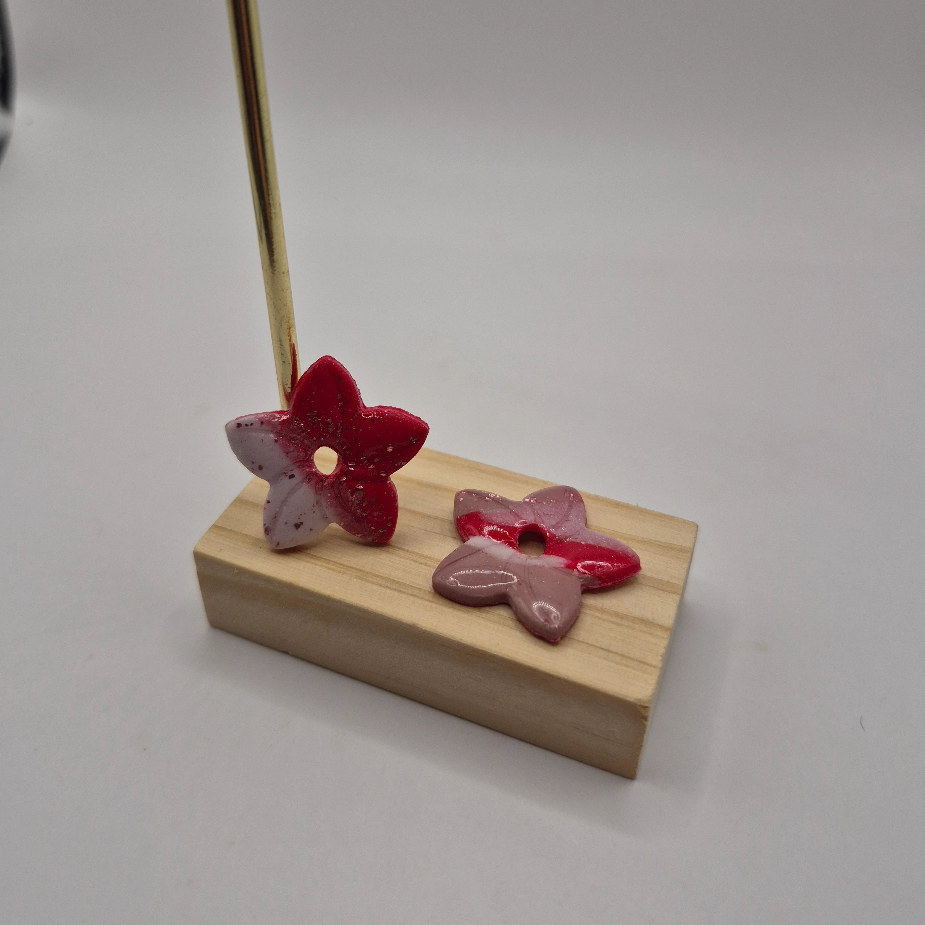 Boucles d’oreilles pampilles en forme de fleur de tiaré, en pâte polymère rose, blanc, rouge, pailletée, faites main avec finition résine, présentées sur un support en bois  — parure artisanale Thalia.