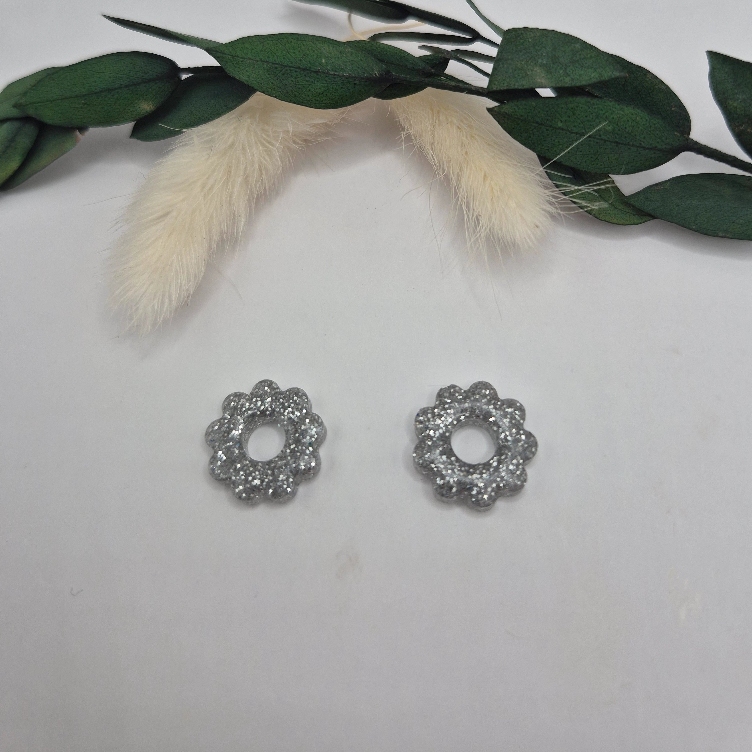 Pampilles argent résine pailleté posées à plat sur surface neutre, branche vertes et pampa en fond de décor