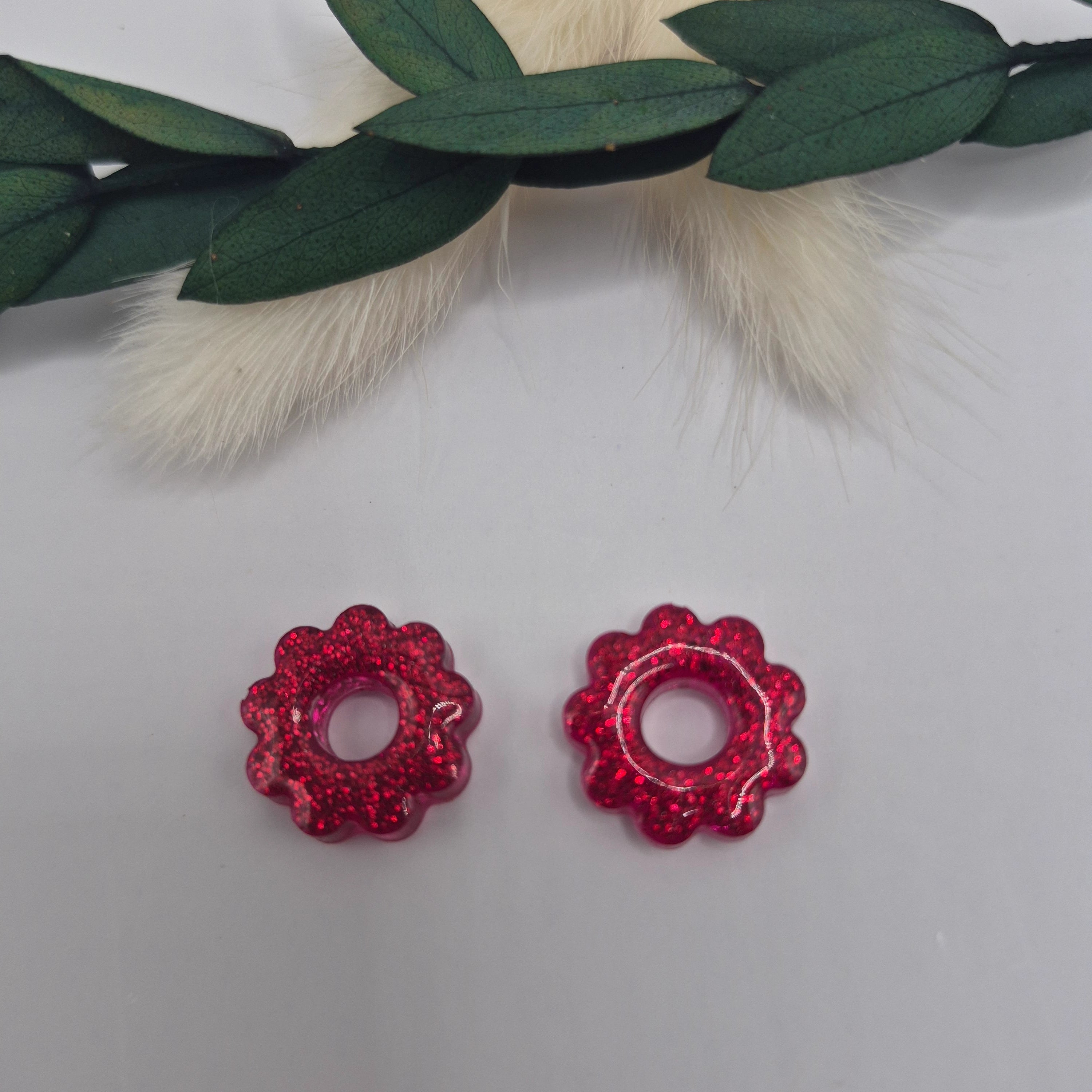 Boucles d’oreilles pampilles rouges Amélie en résine époxy pailletée posées à plat sur fond neutre avec branche de pampa et feuilles au dessus en décor