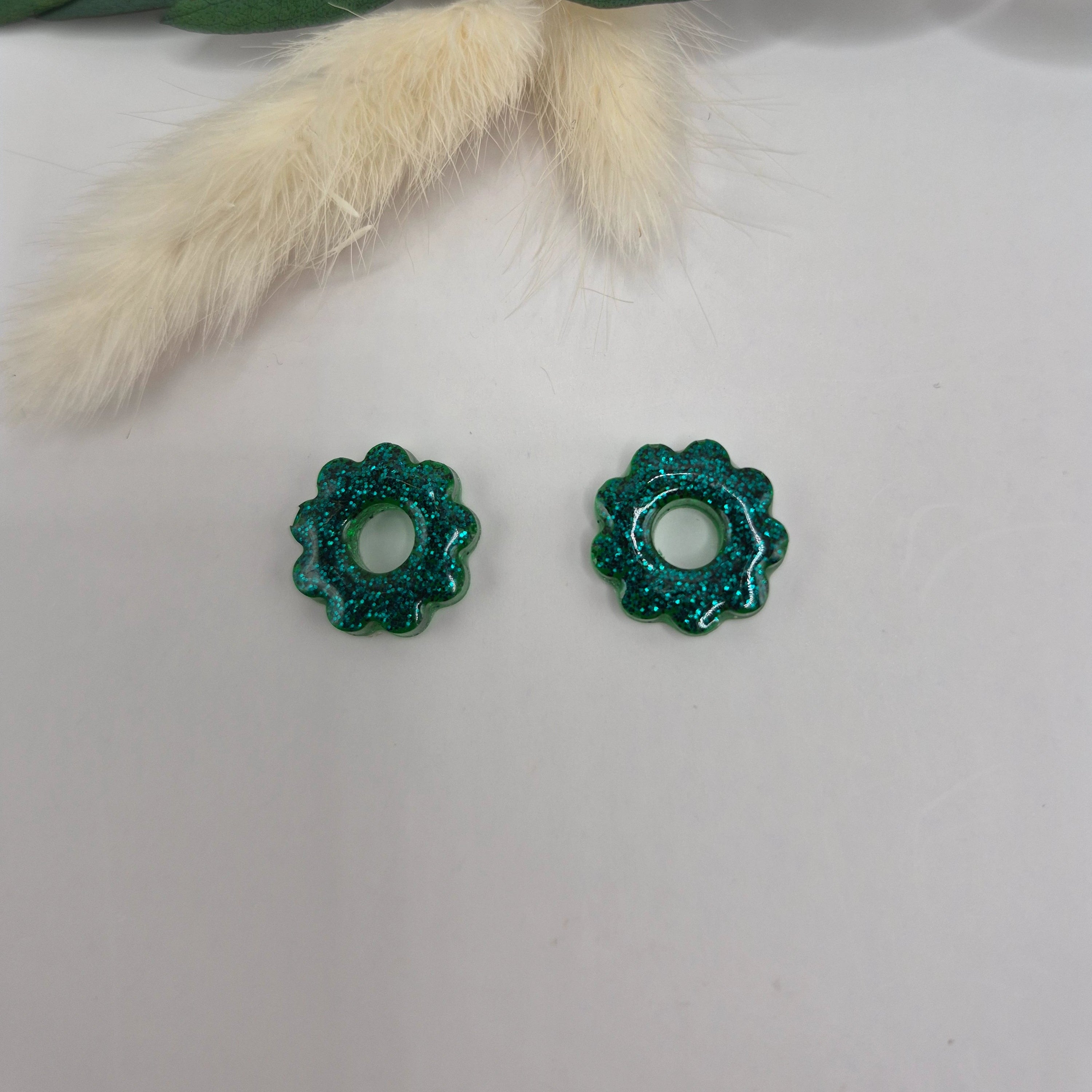 Pampilles vertes résine pailletée posées à plat sur surface neutre avec branche feuilles vertes et pampa en fond de décor 