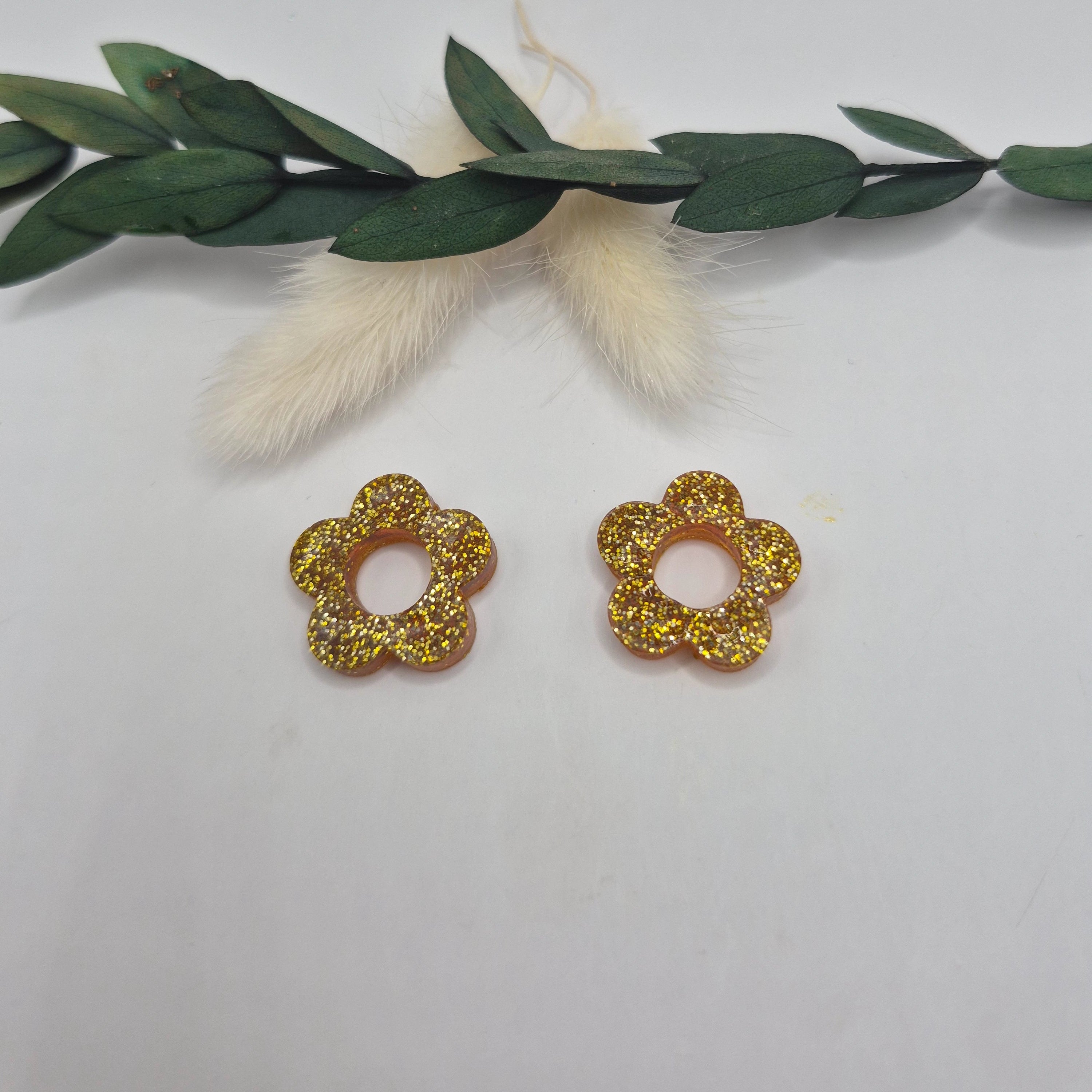 Pampilles Lexie dorées résine pailletée posées à plat avec branche verte et pampa en fond de décor