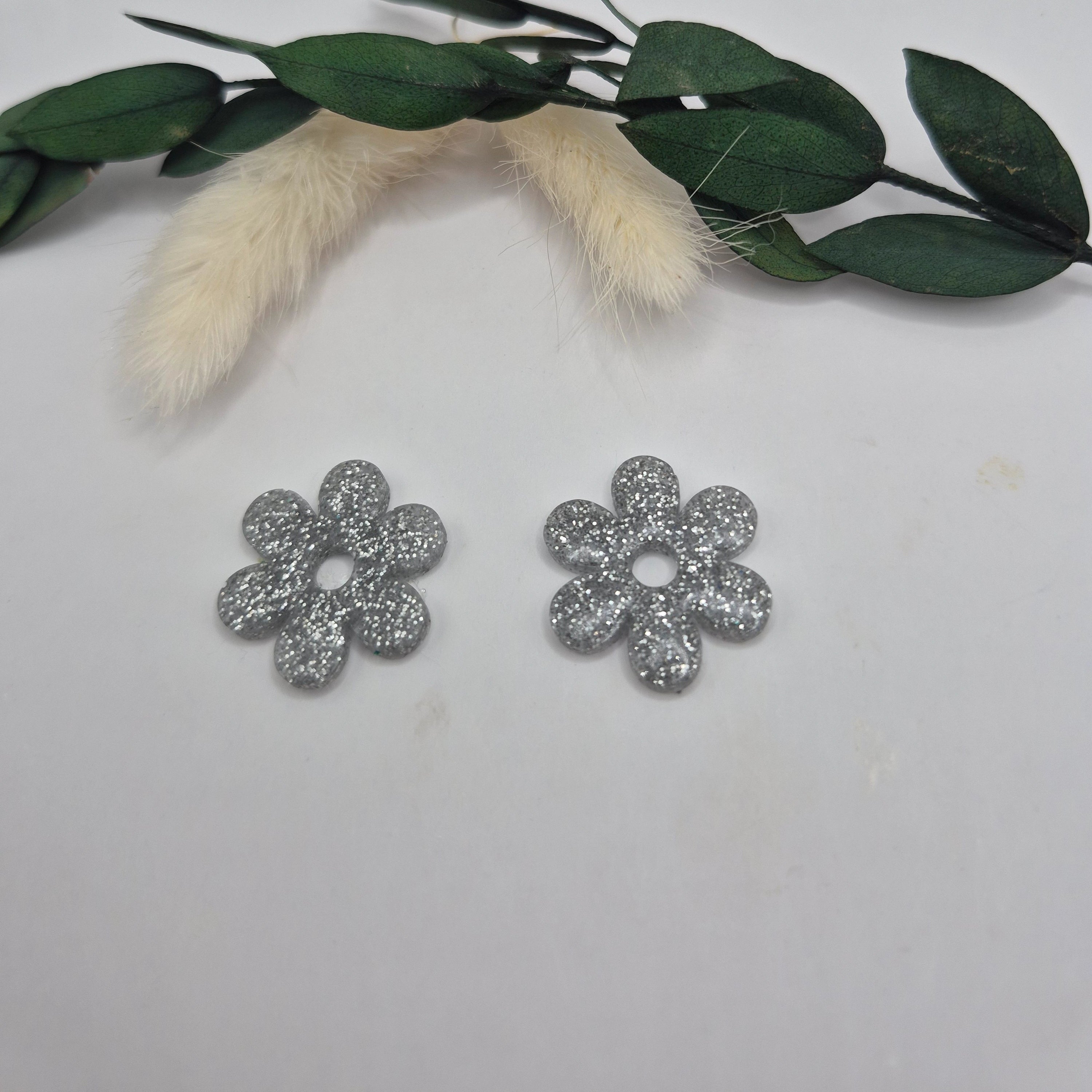 Pampilles argent Marjorie résine pailletée posées à plat avec branche verte et pampa en fond de décor