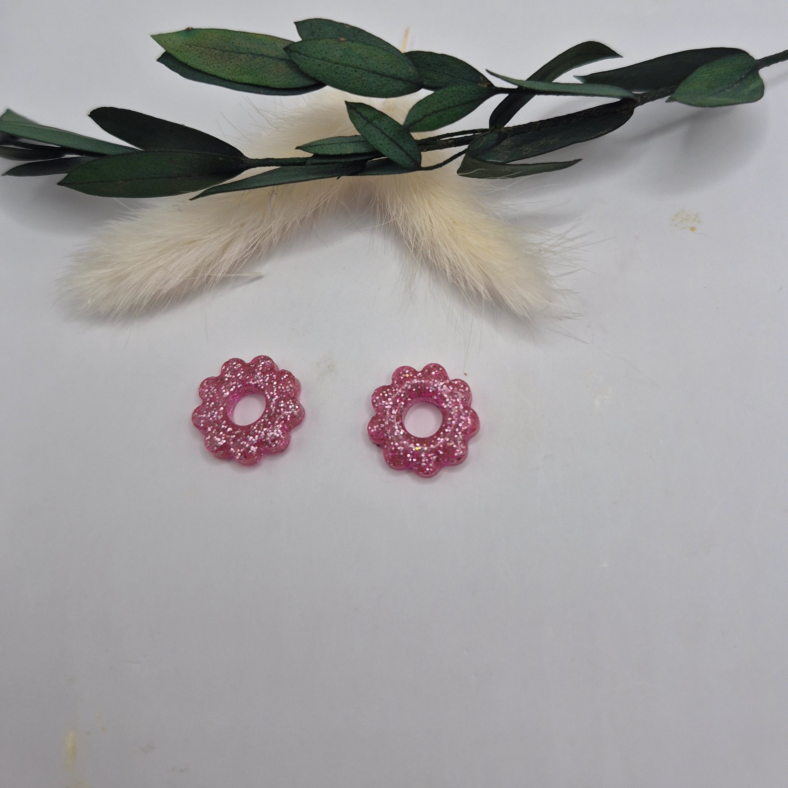 Pampilles roses résine pailleté sur créoles posées à plat avec branche verte et pampa en fond de décor