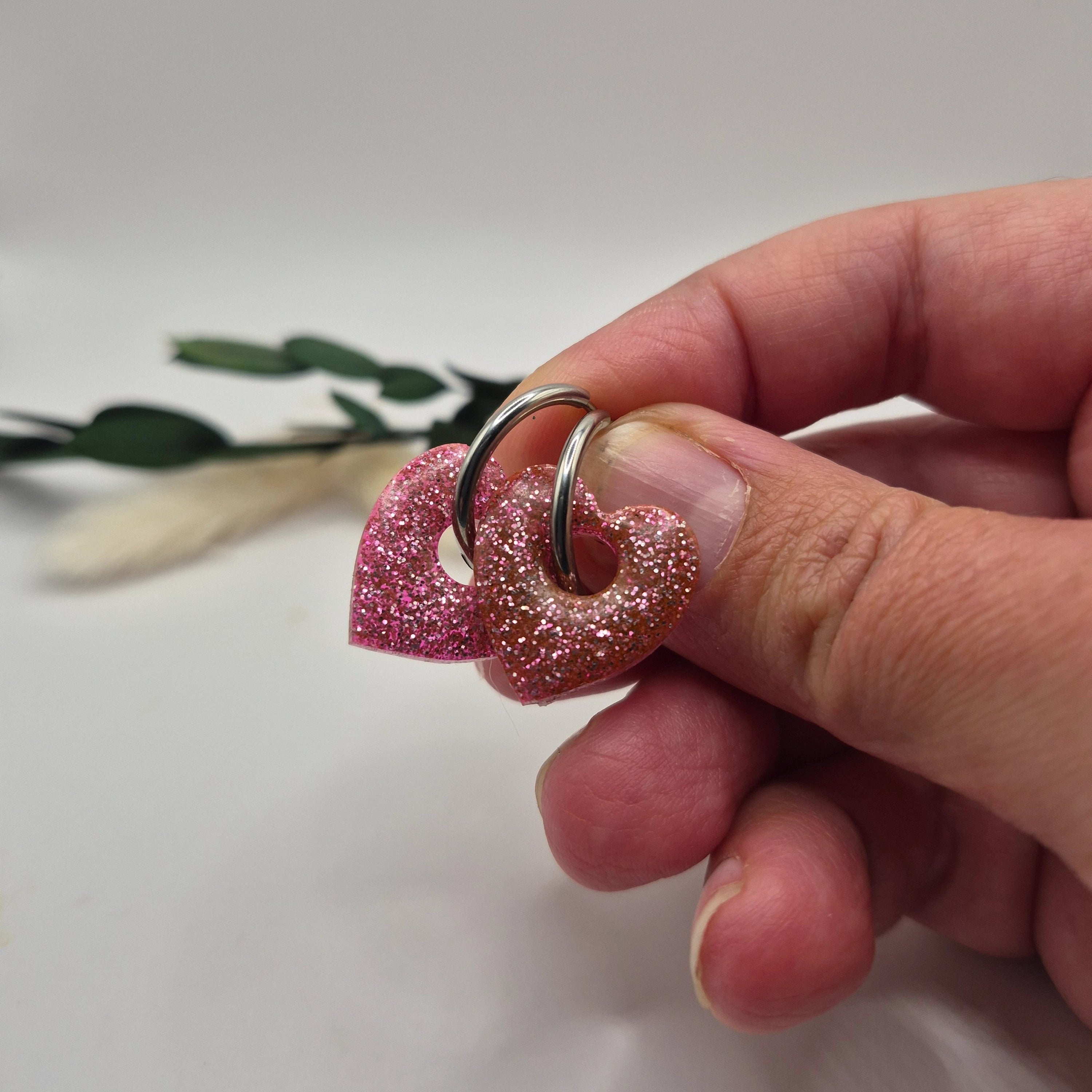 Pampilles Coralie roses résine pailleté sur créoles inoxydables argentées tenues à la main avec branche verte et pampa en fond de décor