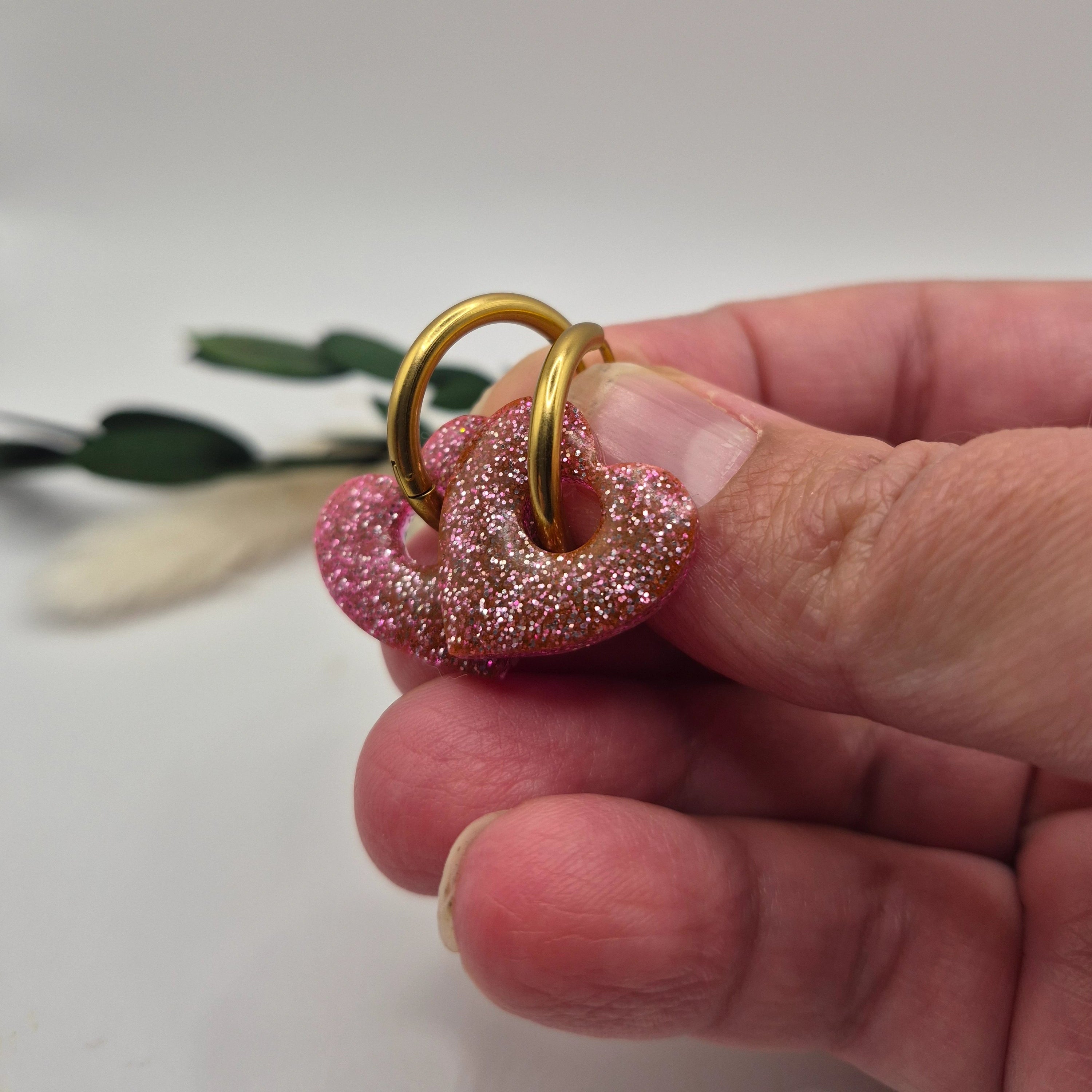 Pampilles Coralie roses résine pailleté sur créoles inoxydables  dorées tenues à la main avec branche verte et pampa en fond de décor