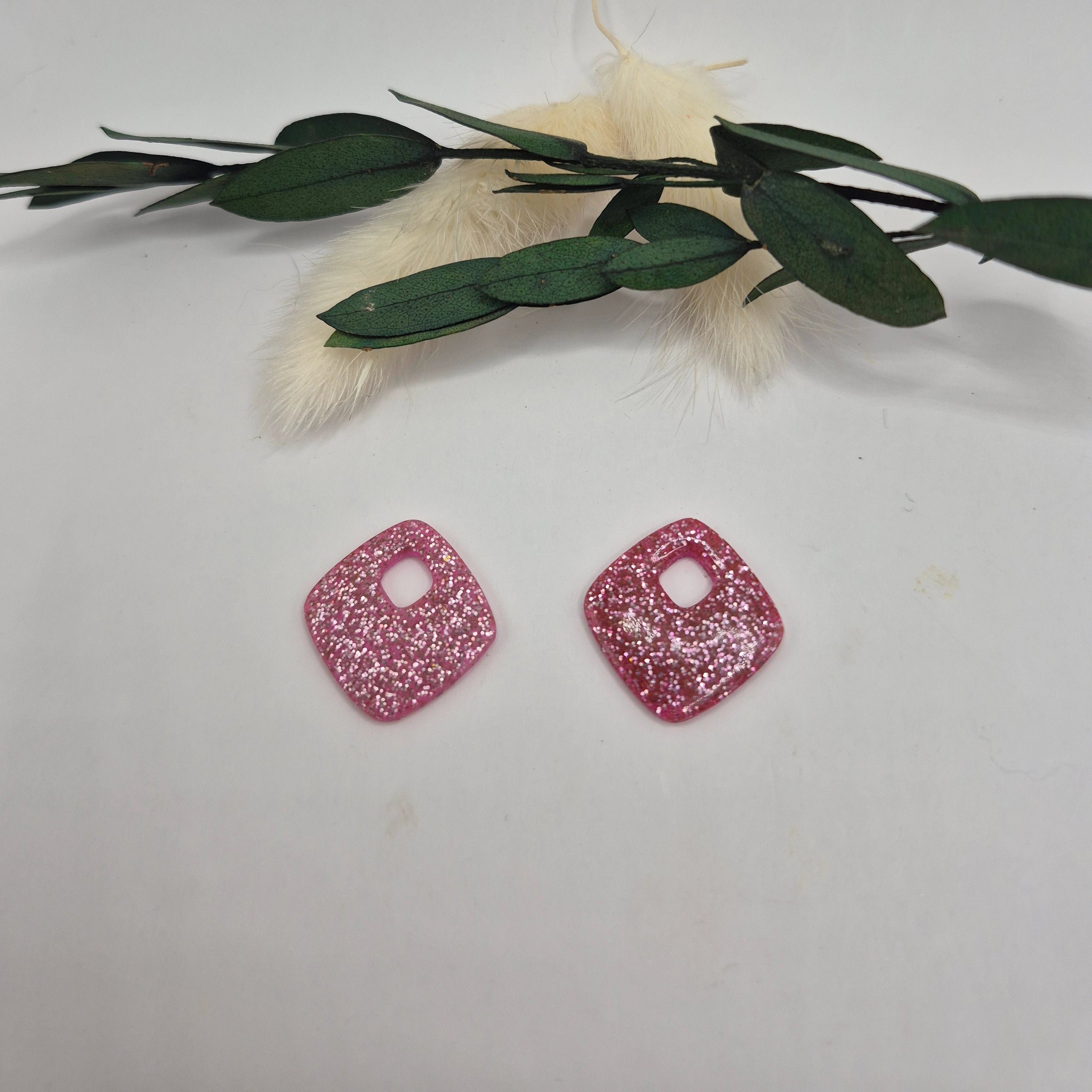 Pampilles Millie losange roses en résine, main tenant les boucles d'oreilles, décor pampa et feuilles vertes